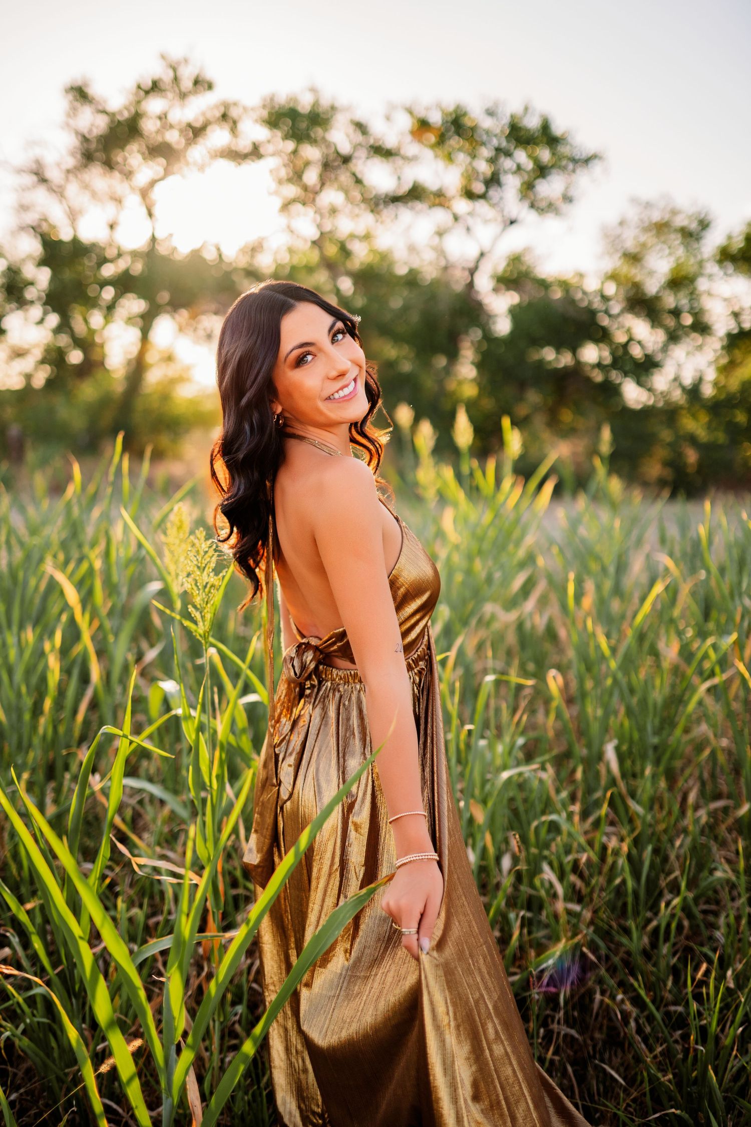 Outdoor portrait session in shimmering dress surrounded by natural grass during sunset.