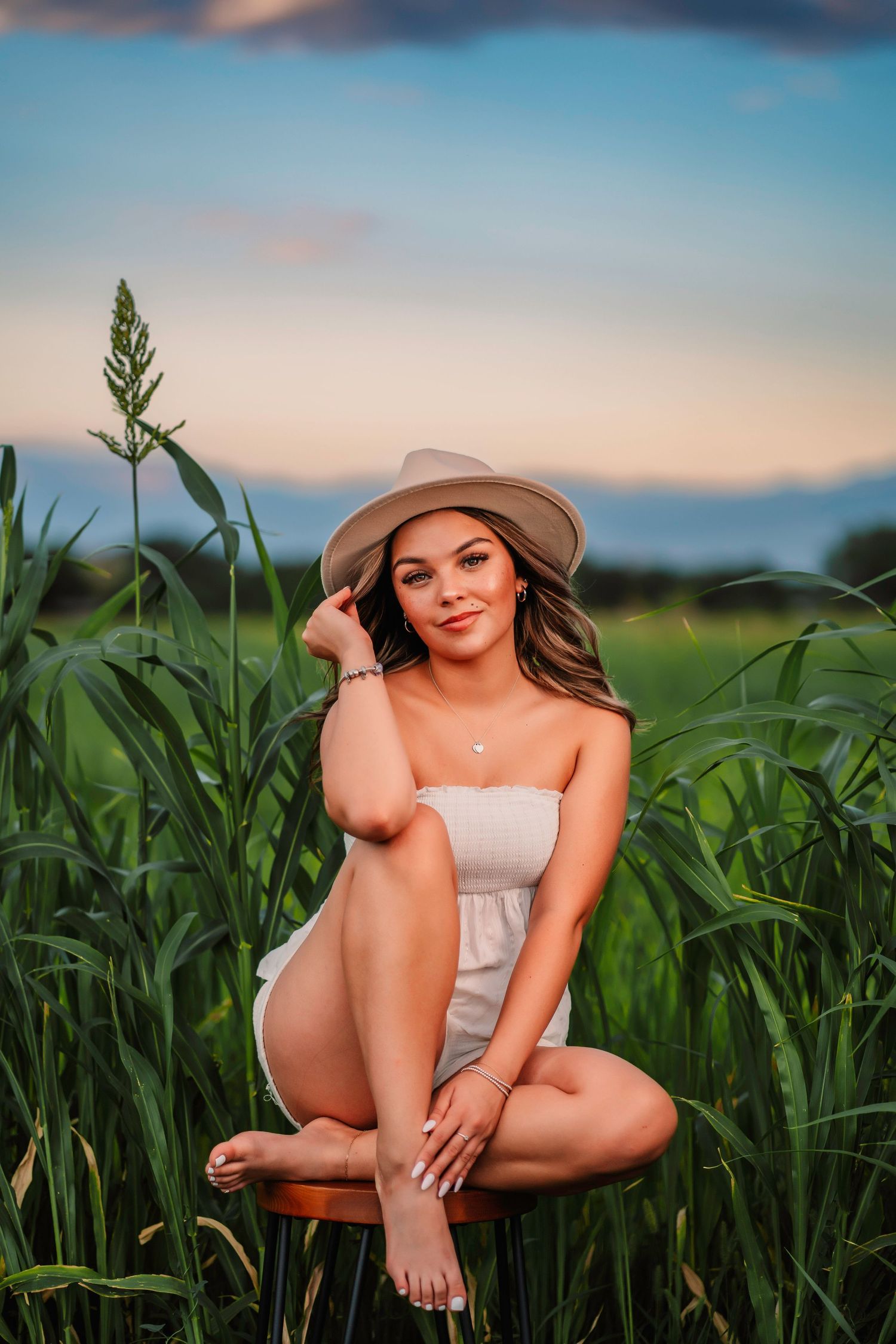 Artistic portrait in cornfield at sunset wearing summer dress and wide-brim hat.