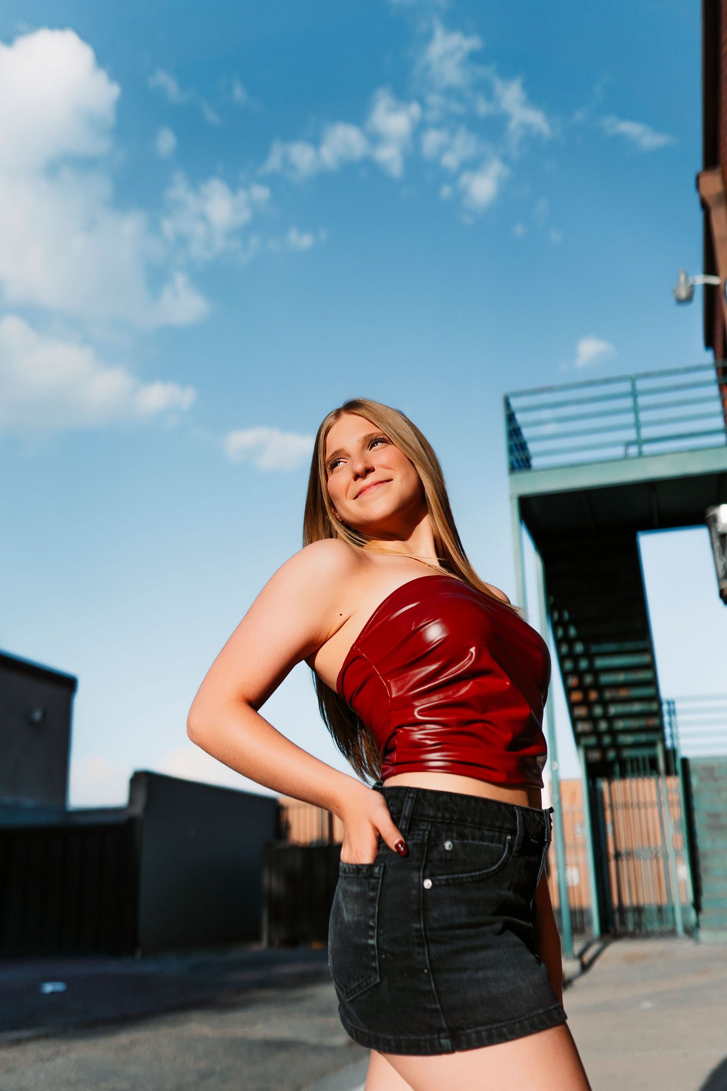 Urban rooftop fashion shoot featuring red top and black denim against bright blue sky.