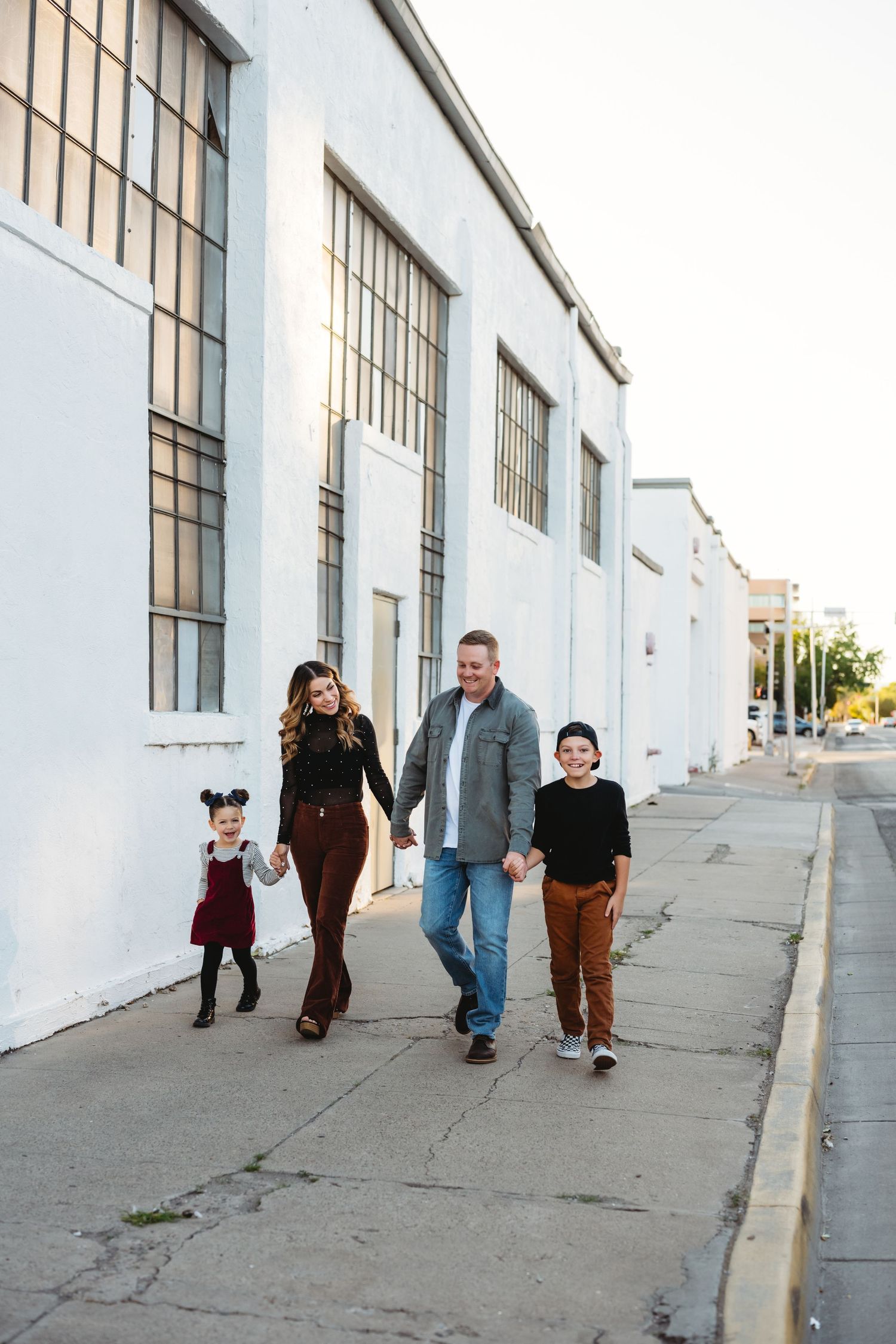 Family walking together along white industrial building exterior.