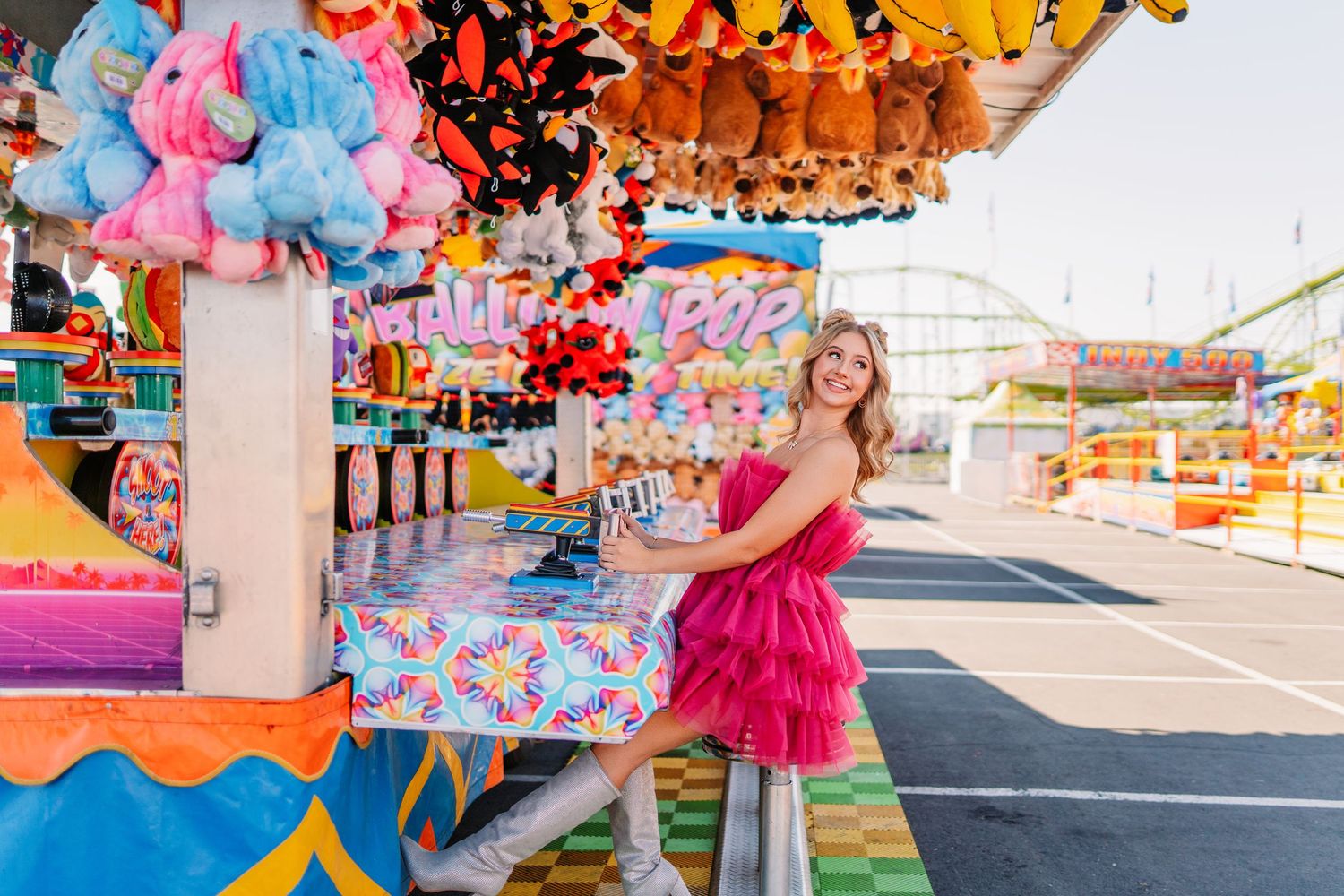 Hot pink tulle dress and silver boots create a playful carnival look against colorful game stalls.