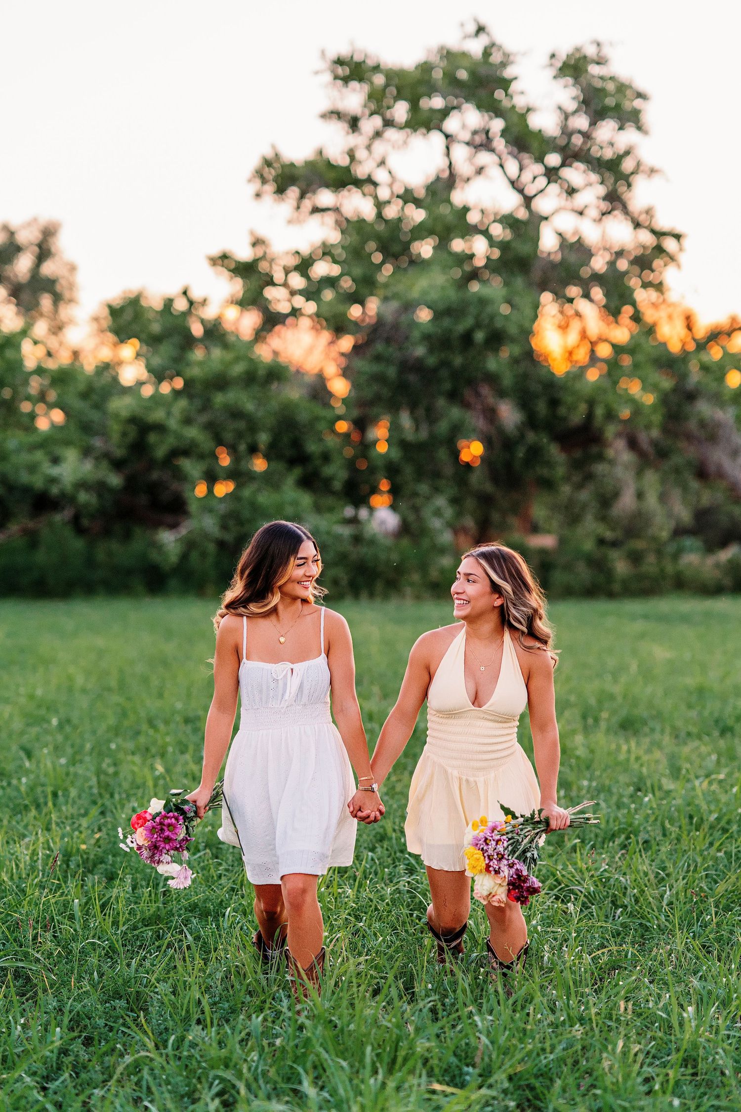 Two people in white summer dresses walk through wildflowers in a sunlit meadow.senior portrait
high school senior
senior photos
senior