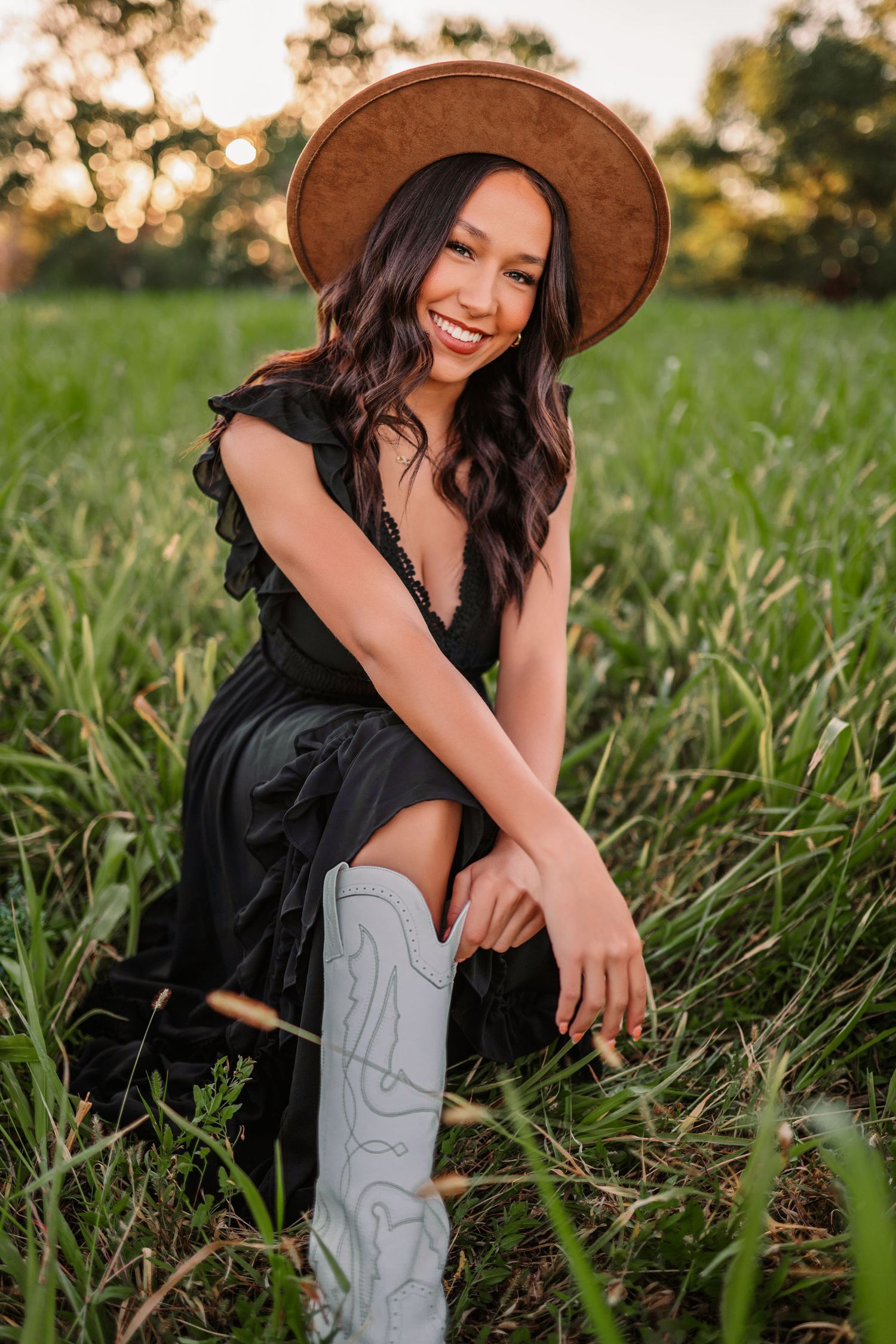 Country style portrait in grass field wearing black dress and brown hat at golden hour.