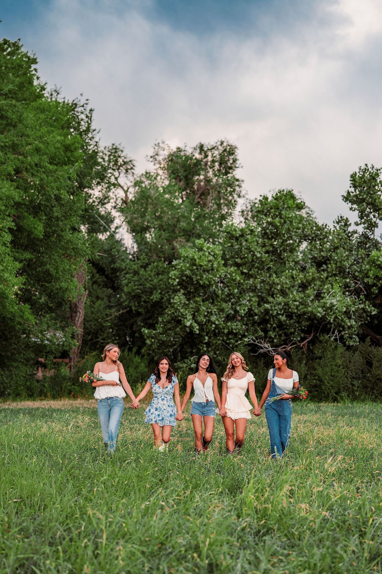 Friends walk together through a lush green field on a cloudy summer day.
