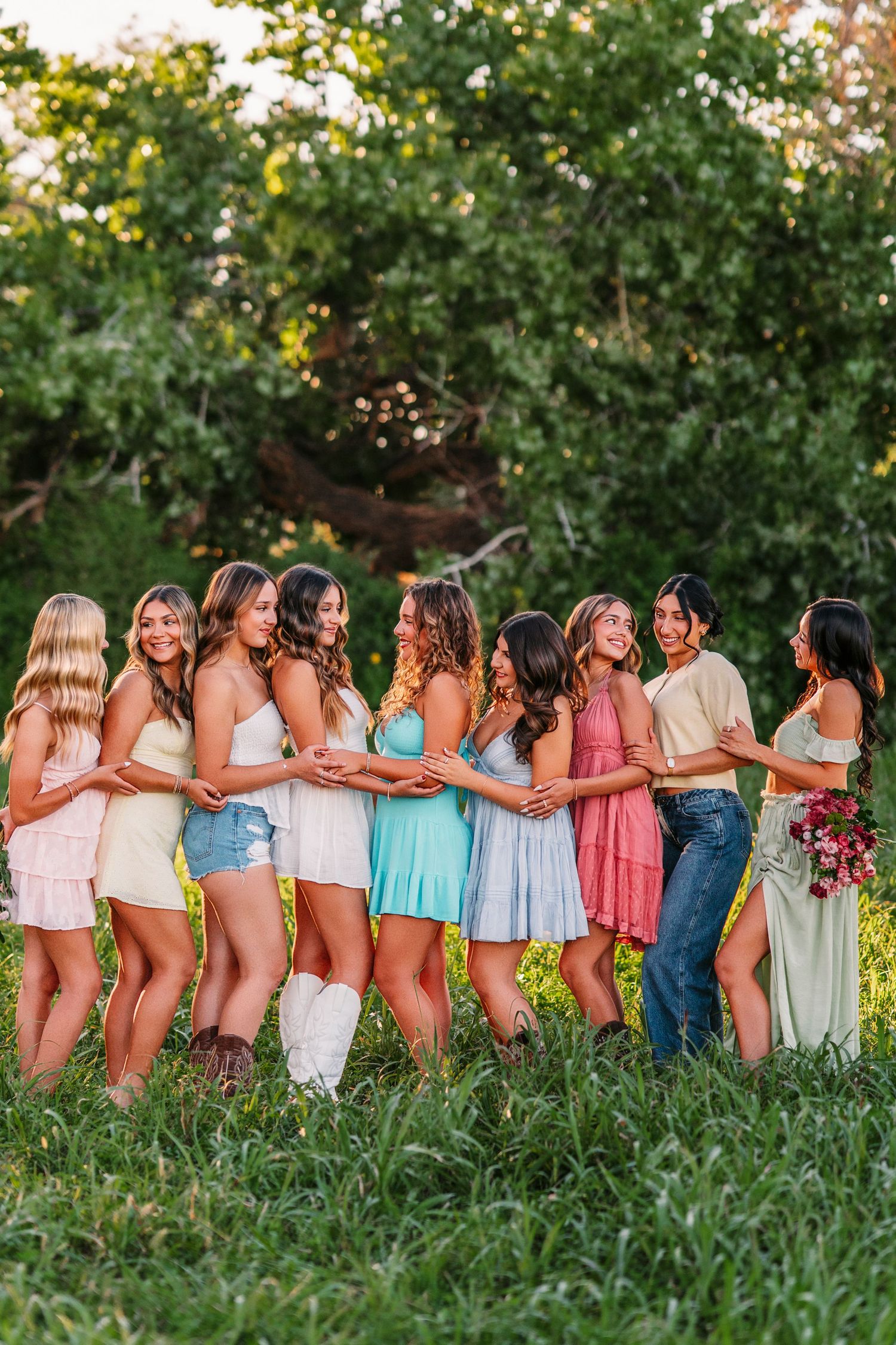 Line of friends posing together in summer outfits against lush green foliage.