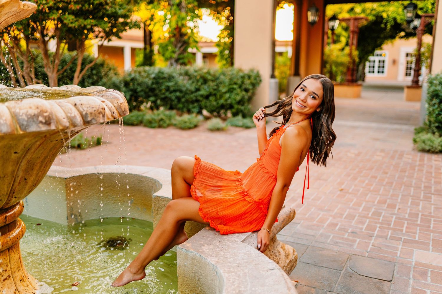 Summer portrait session by a fountain with warm sunset lighting.