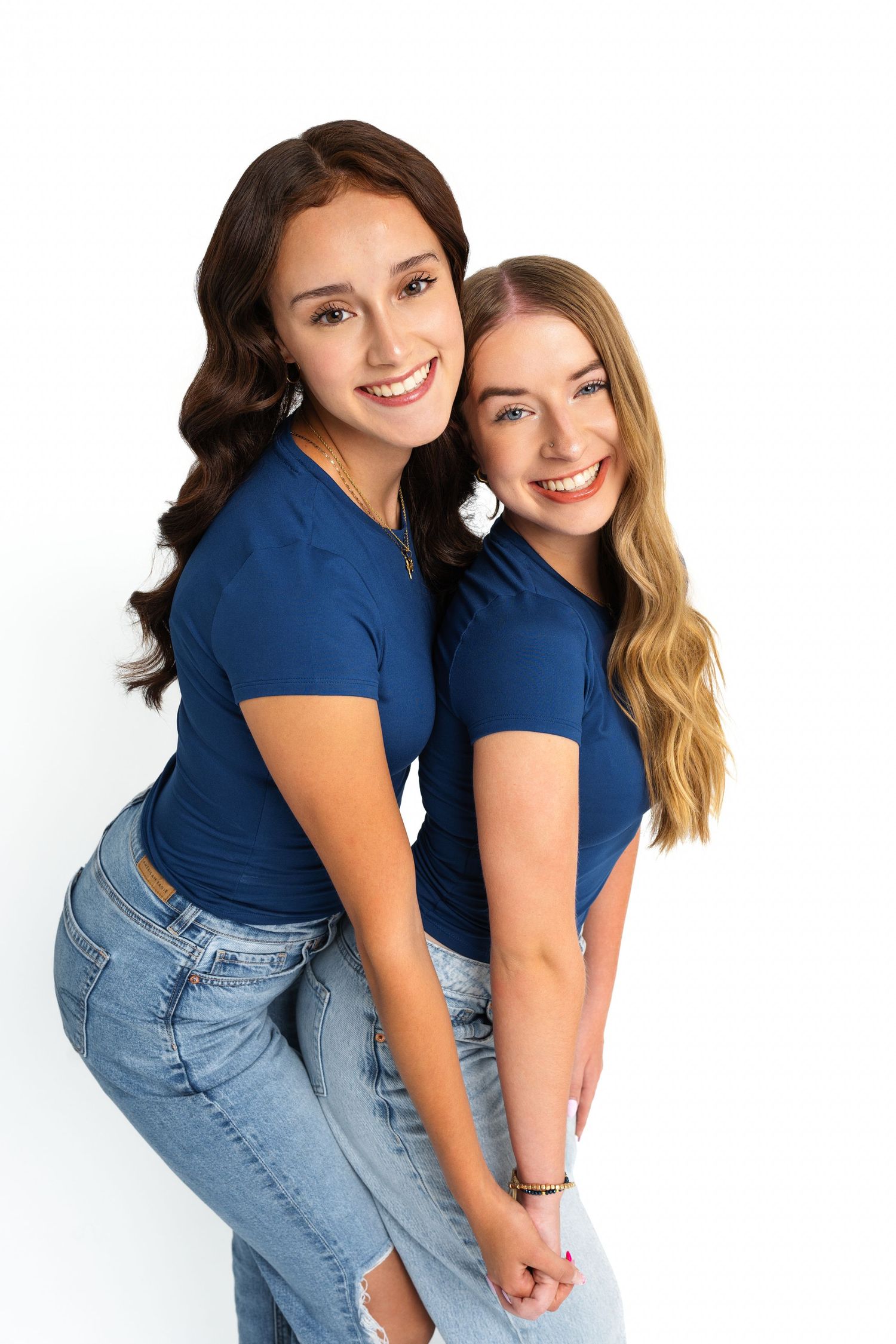 Friends in matching navy tops and jeans pose playfully against white background.
