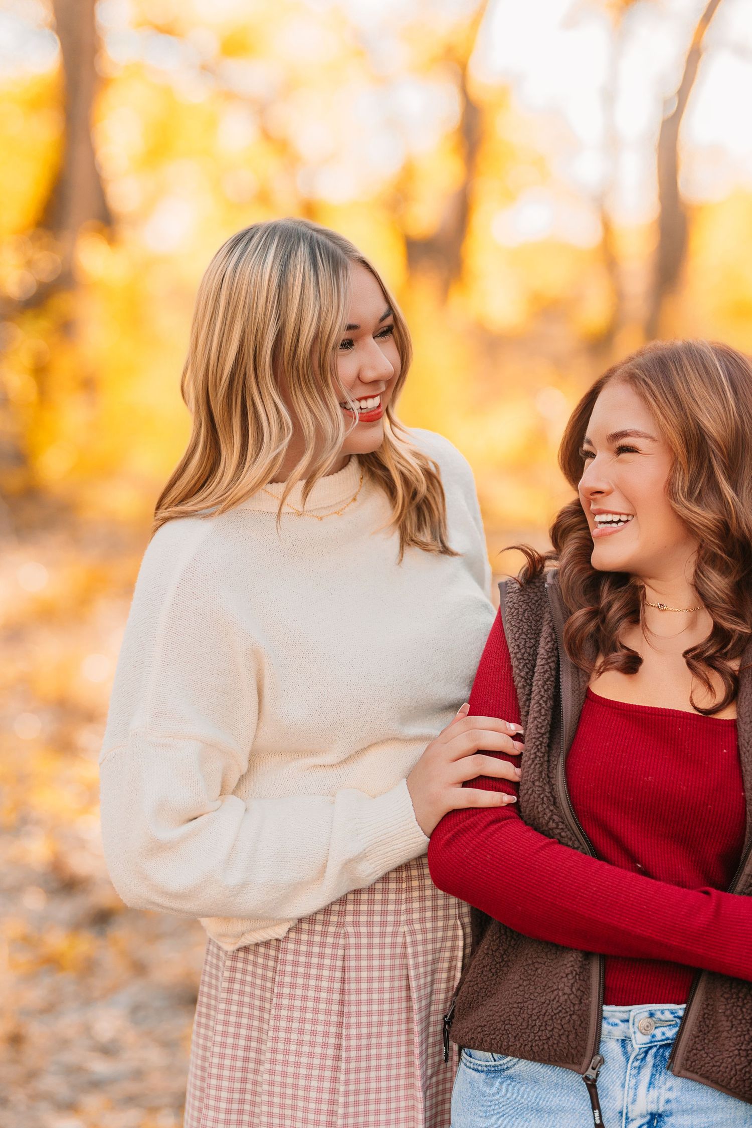 Friends share joyful laughter while posing together in cozy sweaters during golden hour.
