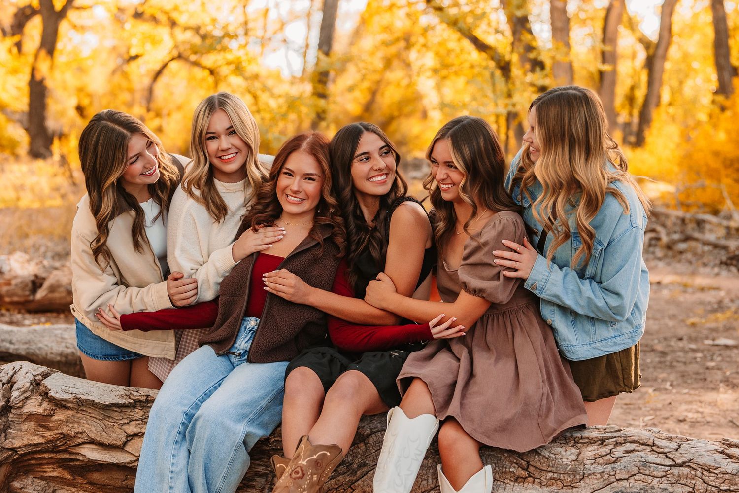Group of friends laughing together on fallen tree during golden autumn afternoon.