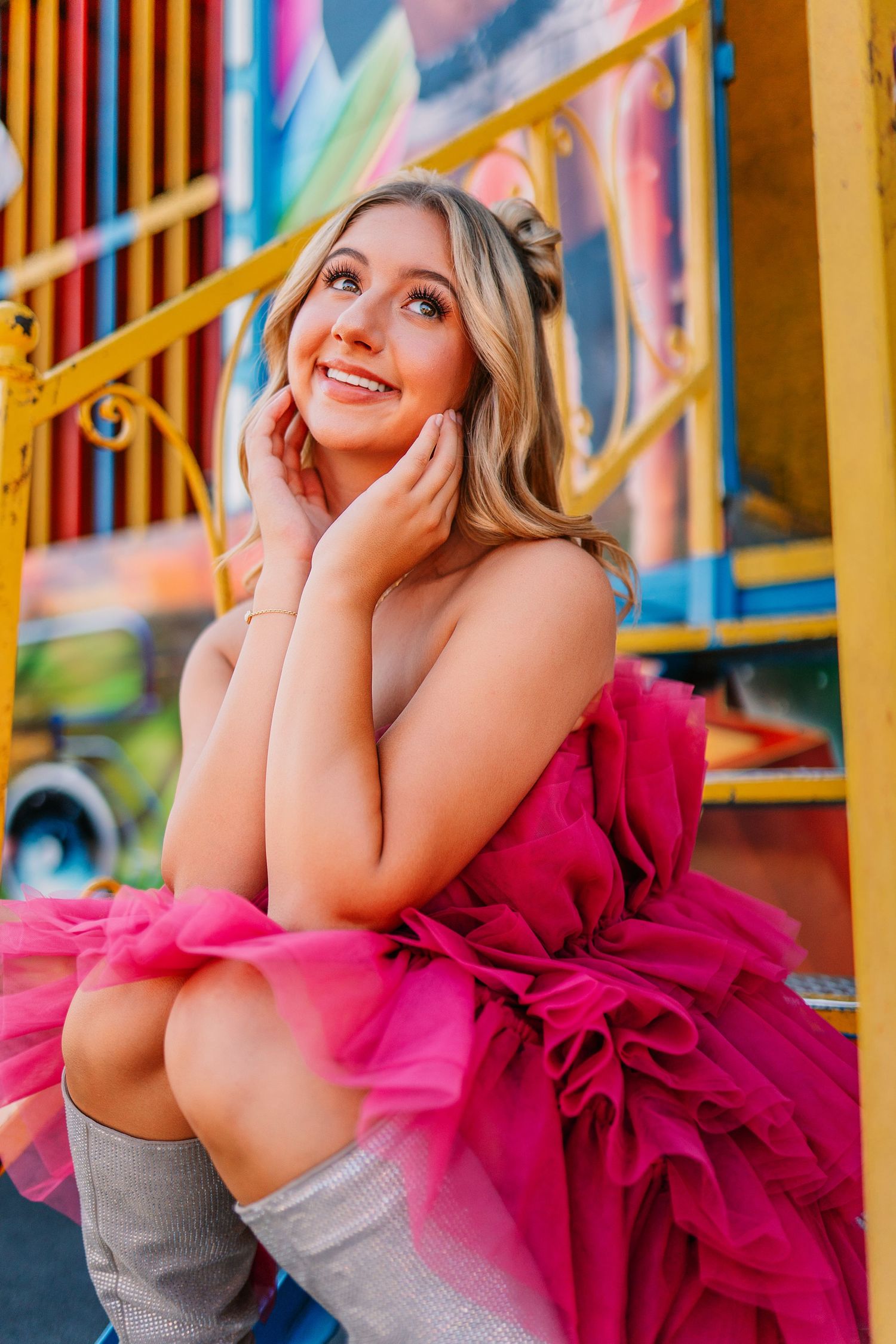 Whimsical carnival photoshoot featuring bright pink ruffled dress against yellow and blue fairground setting.