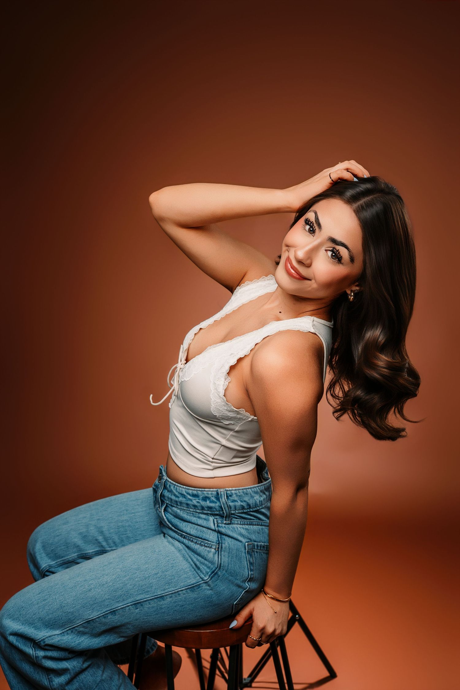 Studio portraits against brown backdrop wearing casual denim and tank top.