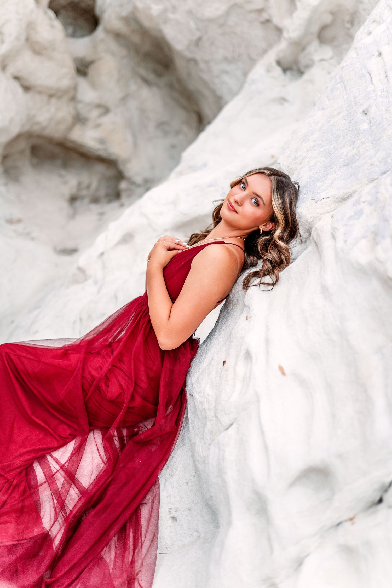 Flowing red dress creates dramatic movement against white rock formations in artistic portraits.