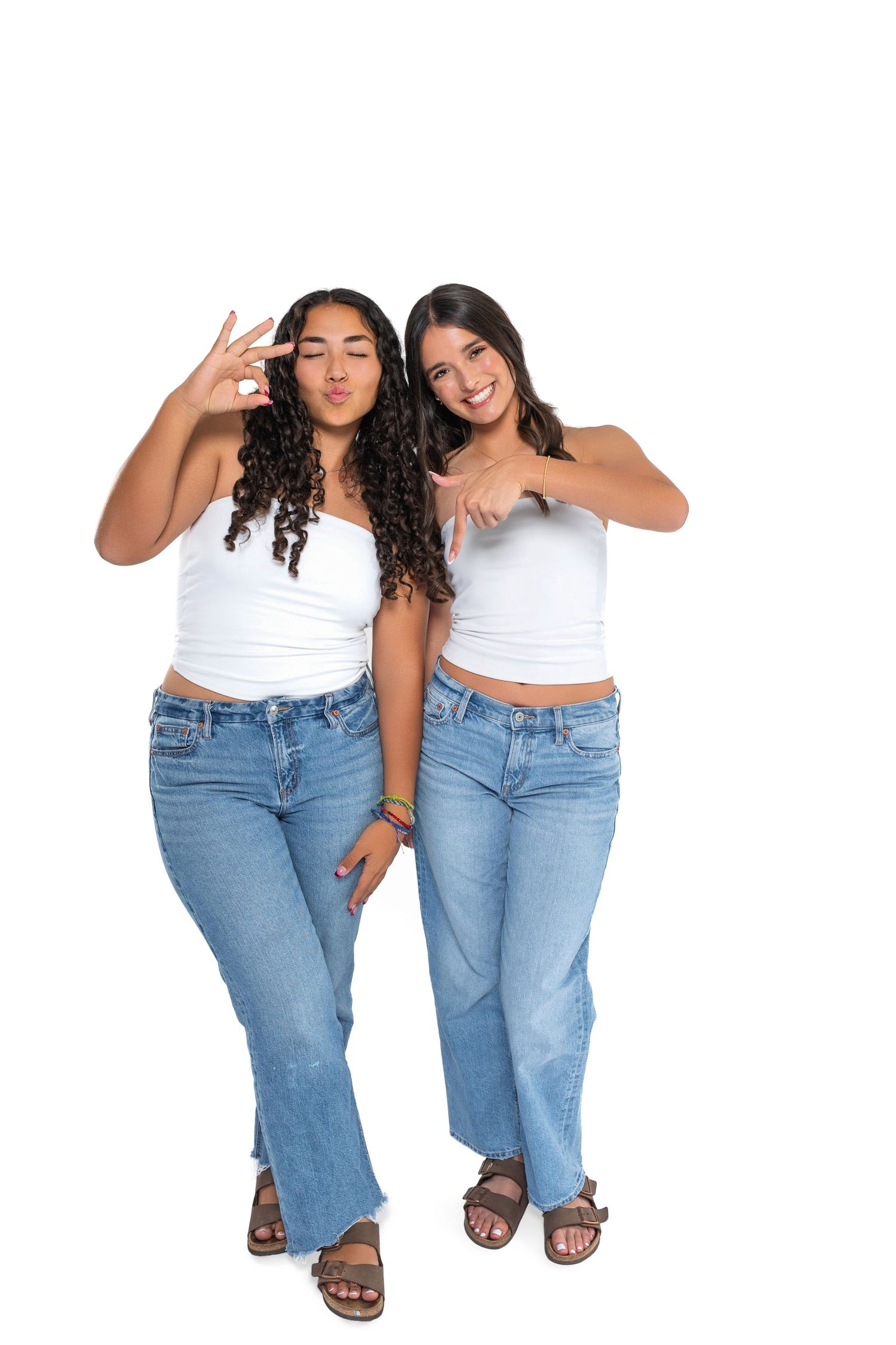 Two friends in matching denim and white tops posing playfully against white background.