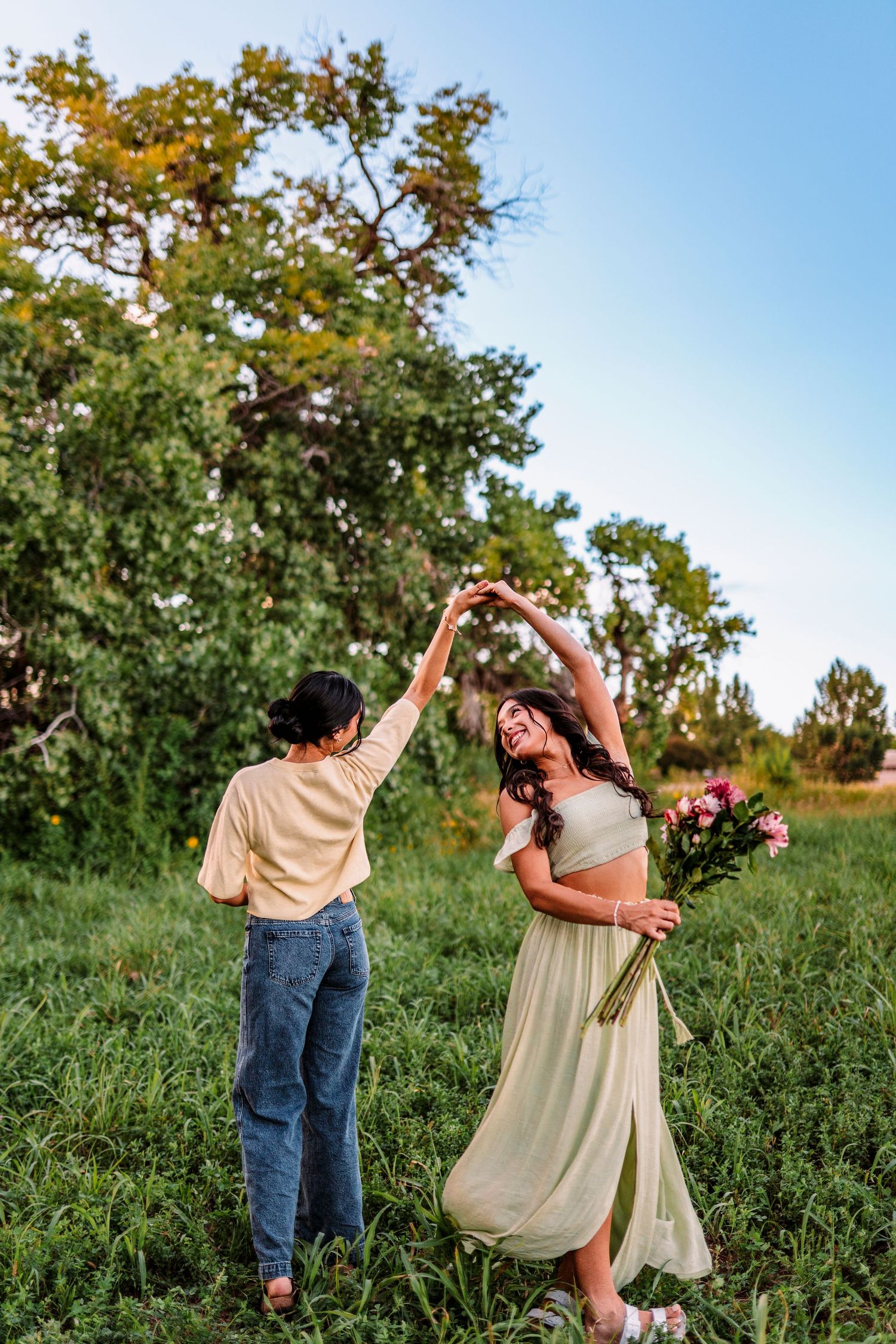 Couple dancing together in a meadow with golden sunlight filtering through trees.