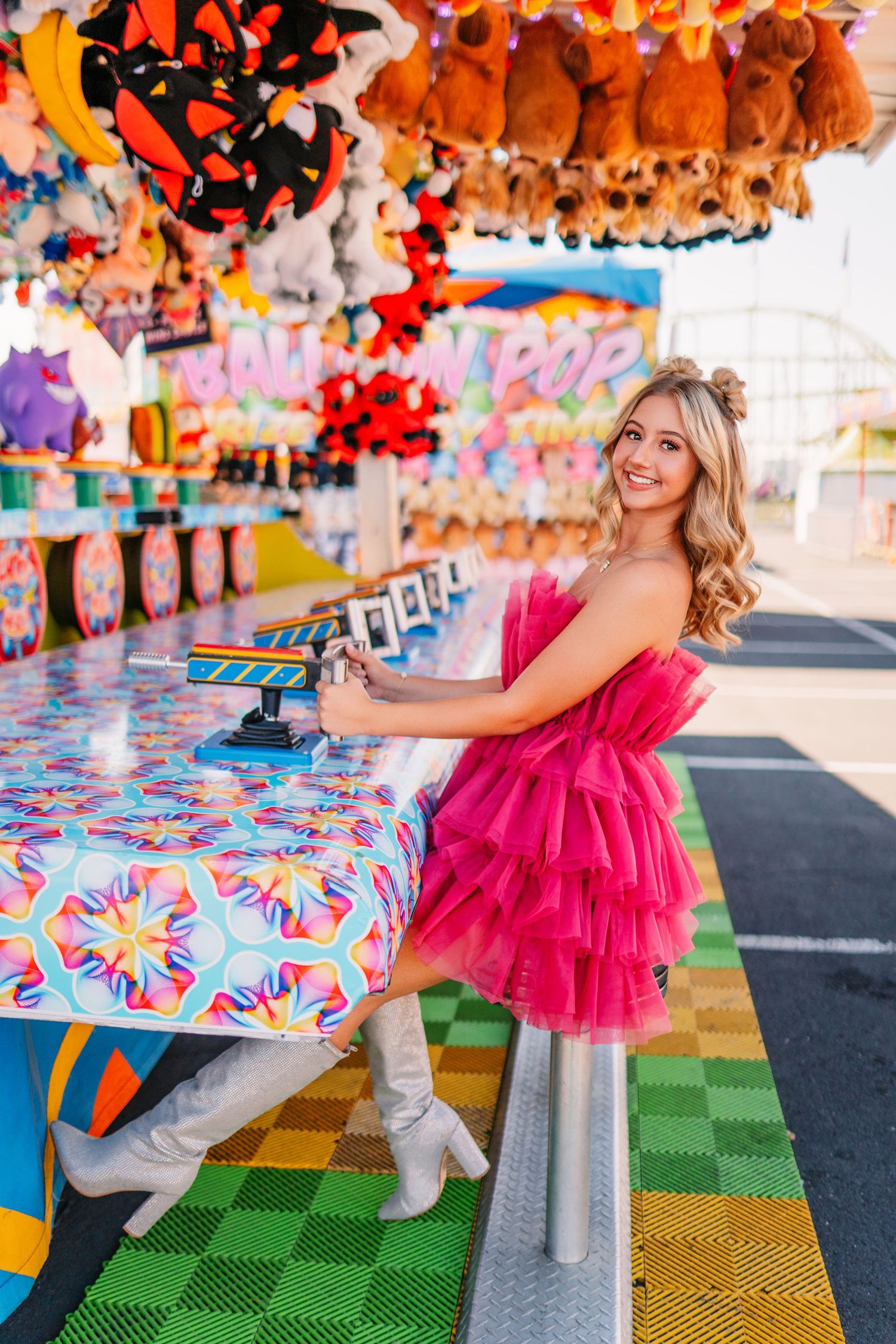 Playful carnival fashion shoot featuring pink tulle dress against colorful game booth with checkered floor.
