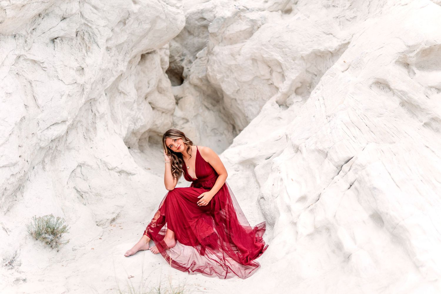 Woman in flowing red dress poses gracefully against white rock formations in desert landscape.