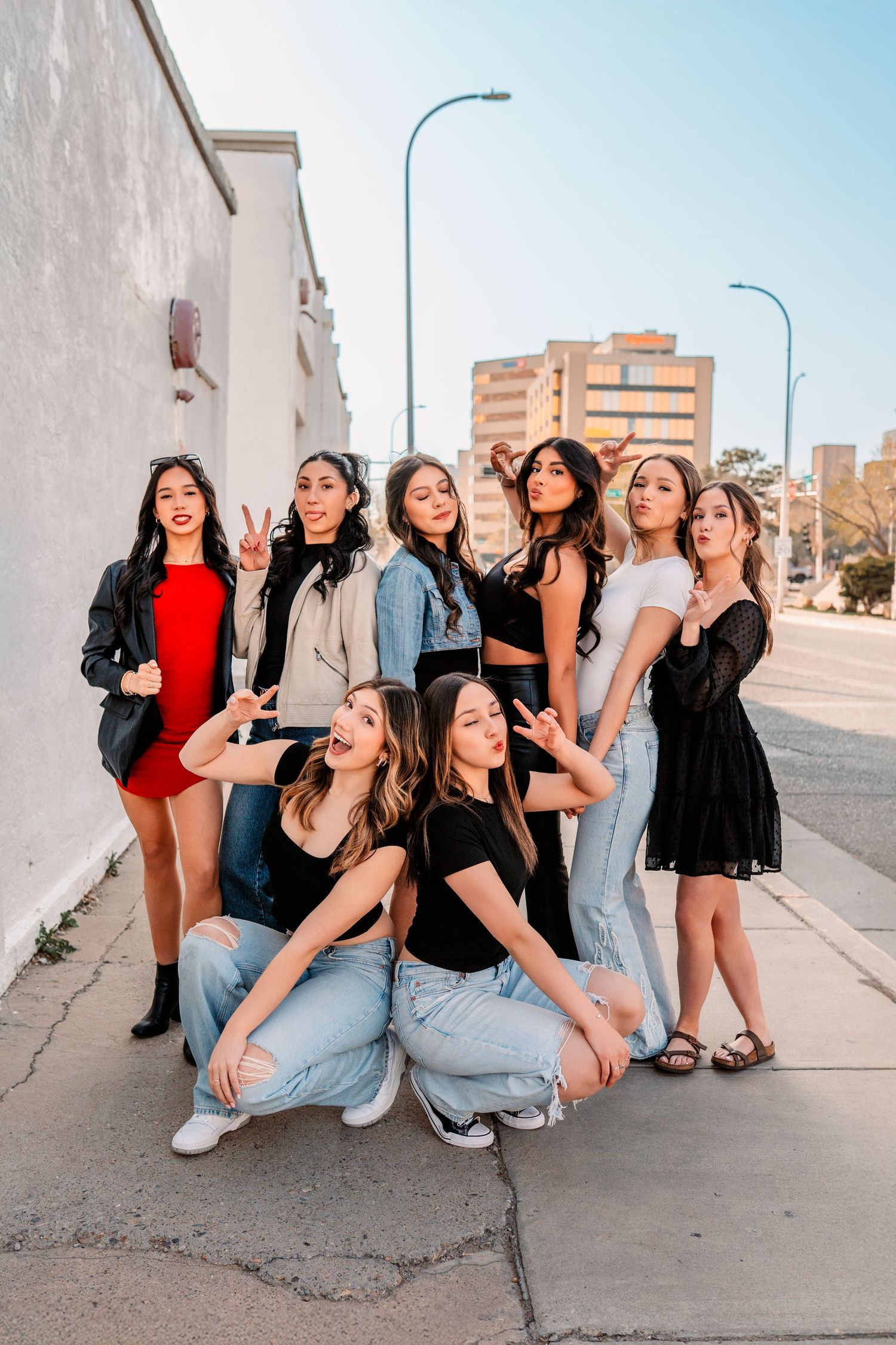 Group strikes fun poses on urban sidewalk wearing mix of casual and dressy outfits.