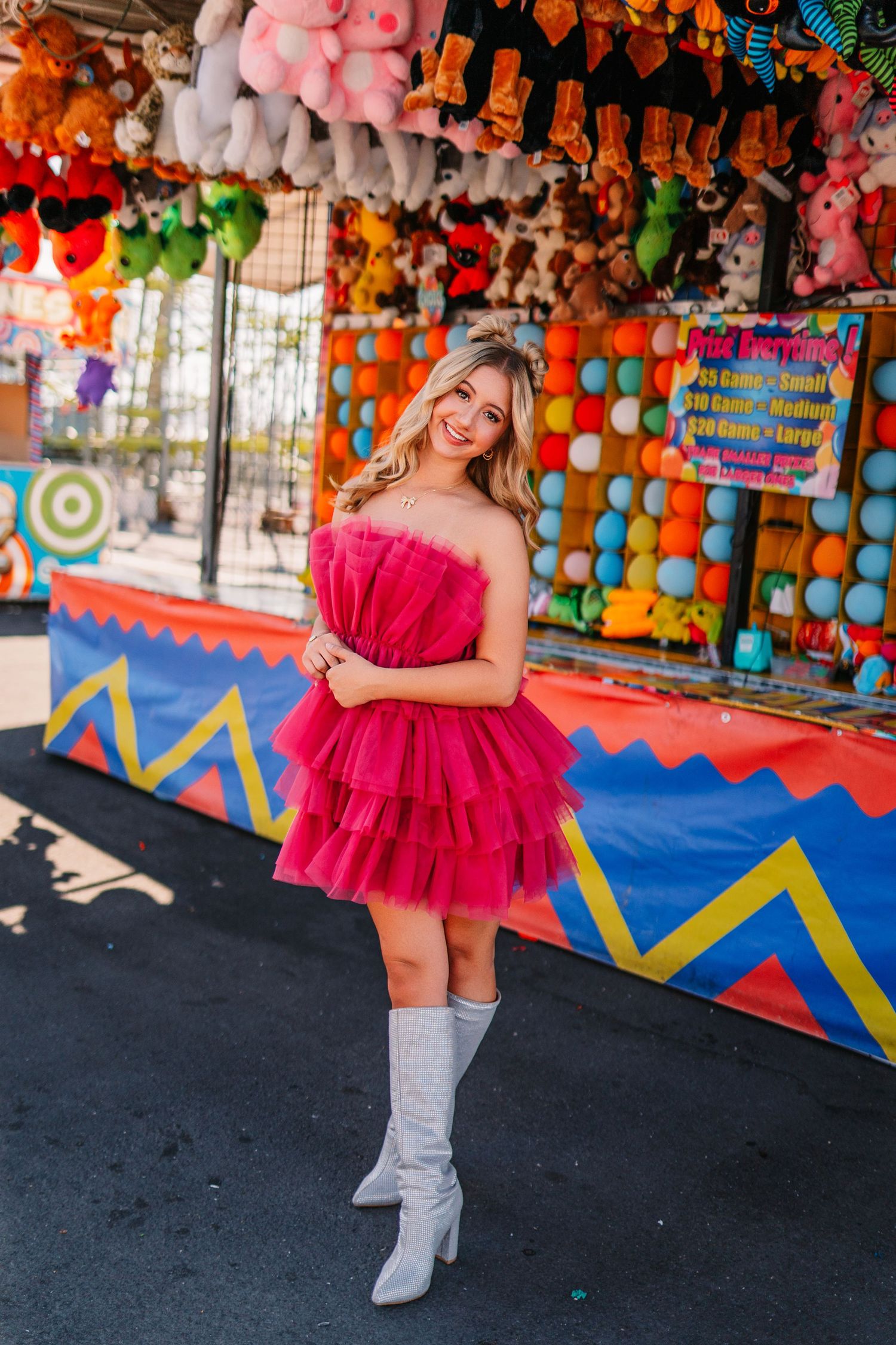 Silver boots and pink dress contrast against vibrant carnival game booths.