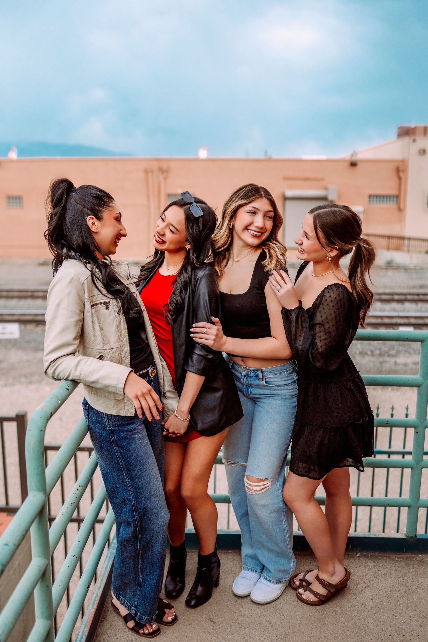 Friends share laughs while hanging out along a turquoise railing at sunset.