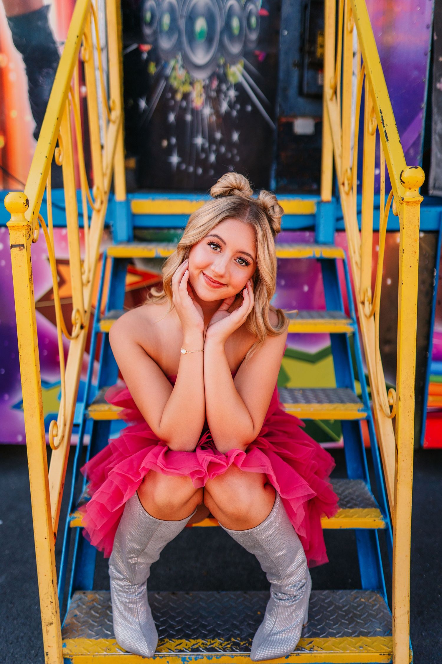 Artistic carnival portrait with hot pink tulle dress and grey boots against colorful fairground structures.