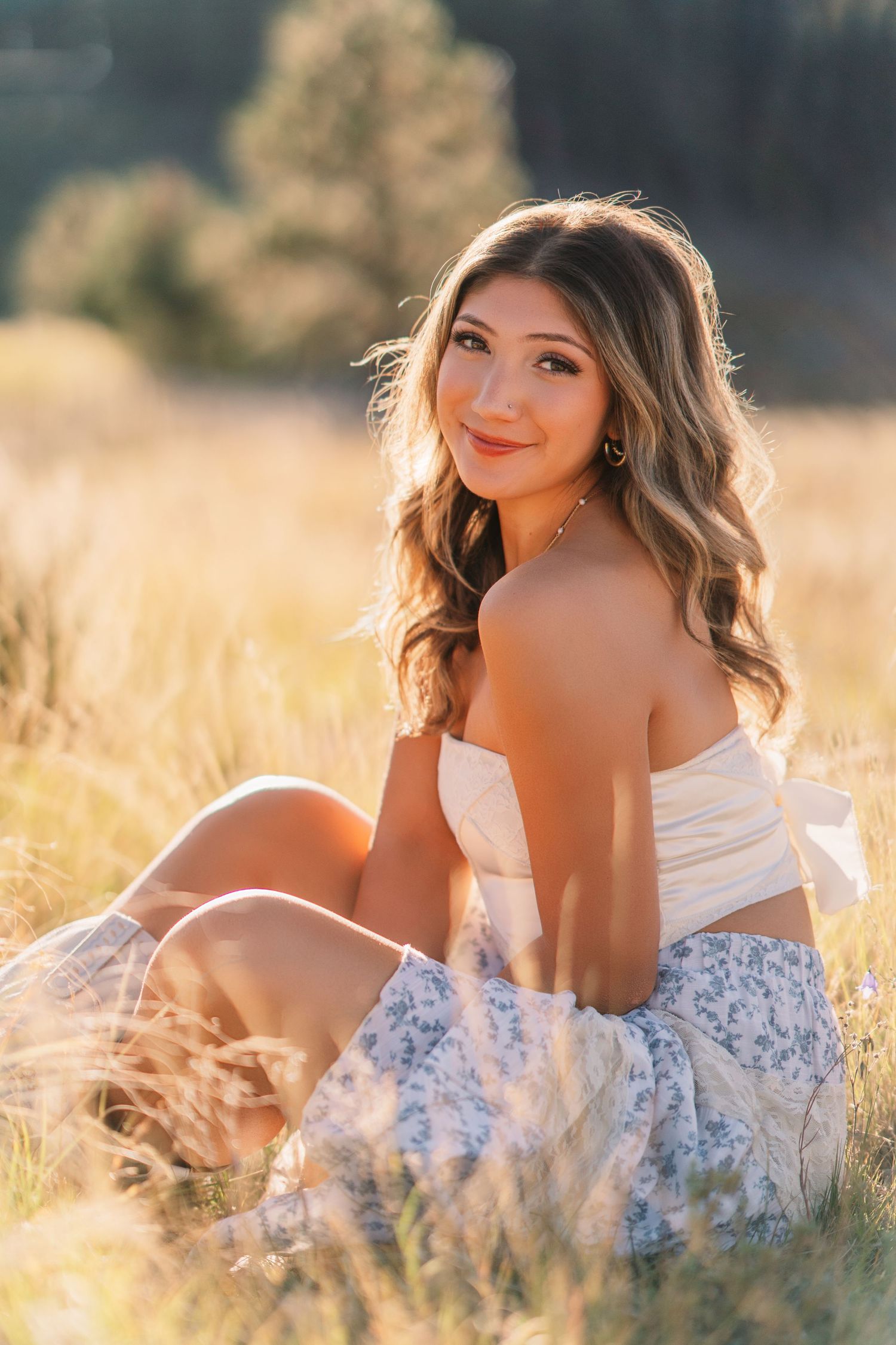 A summer portrait of someone sitting in a sun-drenched field wearing white and floral clothing.