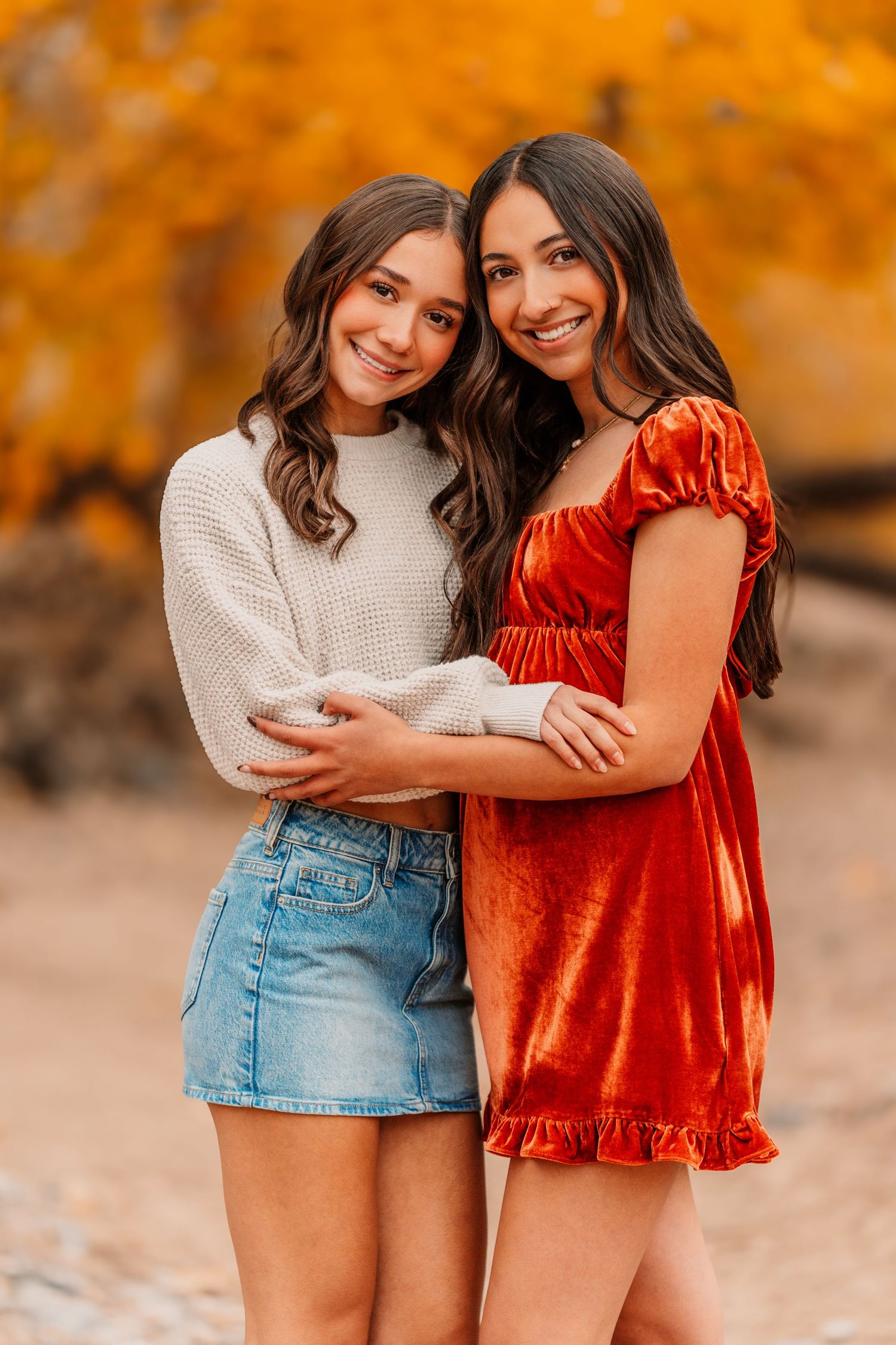 Friends in autumn outfits embrace and laugh against warm orange background.