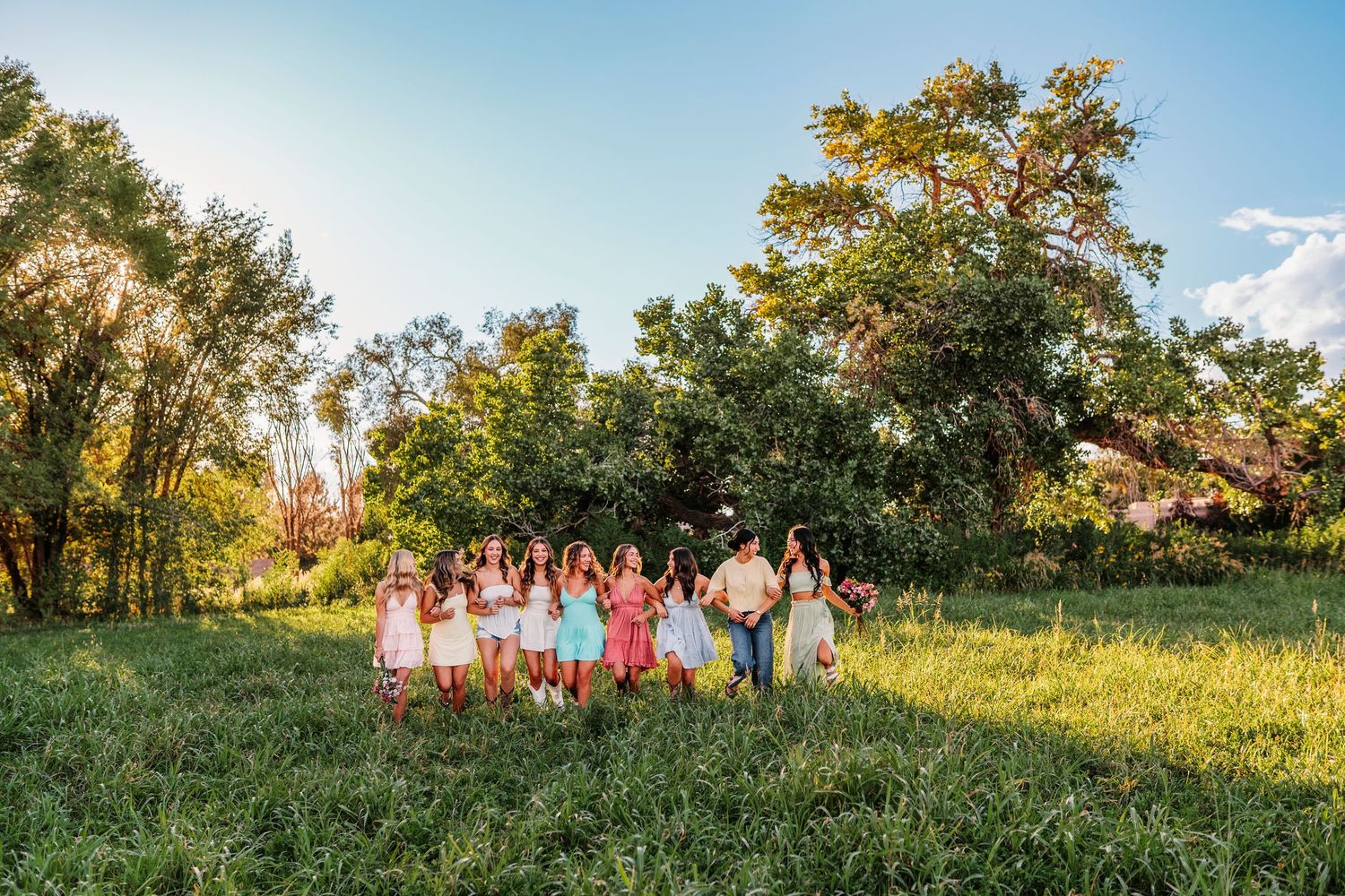 A group poses together in a sunlit meadow with trees and blue sky in the background.