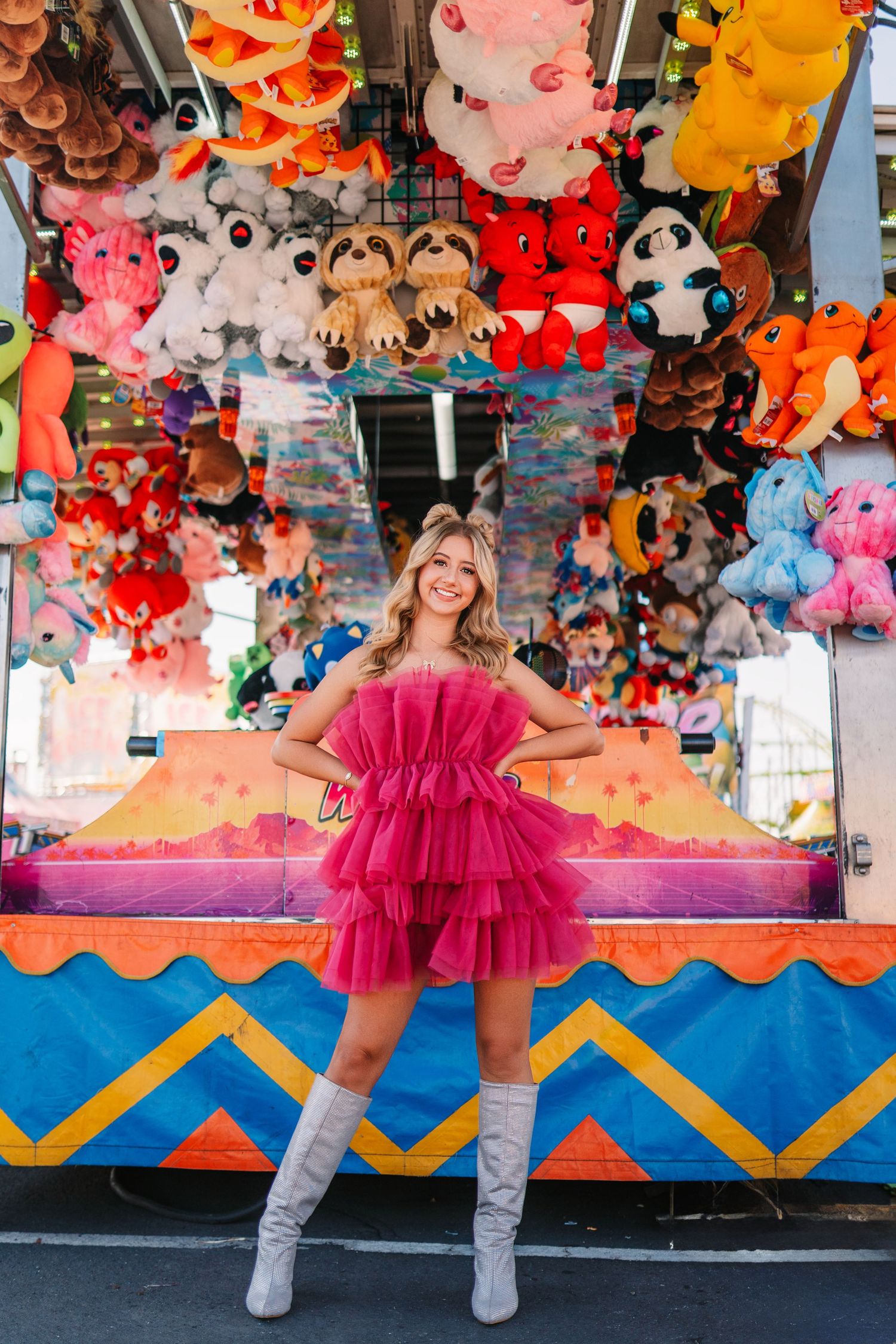 Fashion portrait at carnival game booth with plush toys and geometric patterns in bright colors.