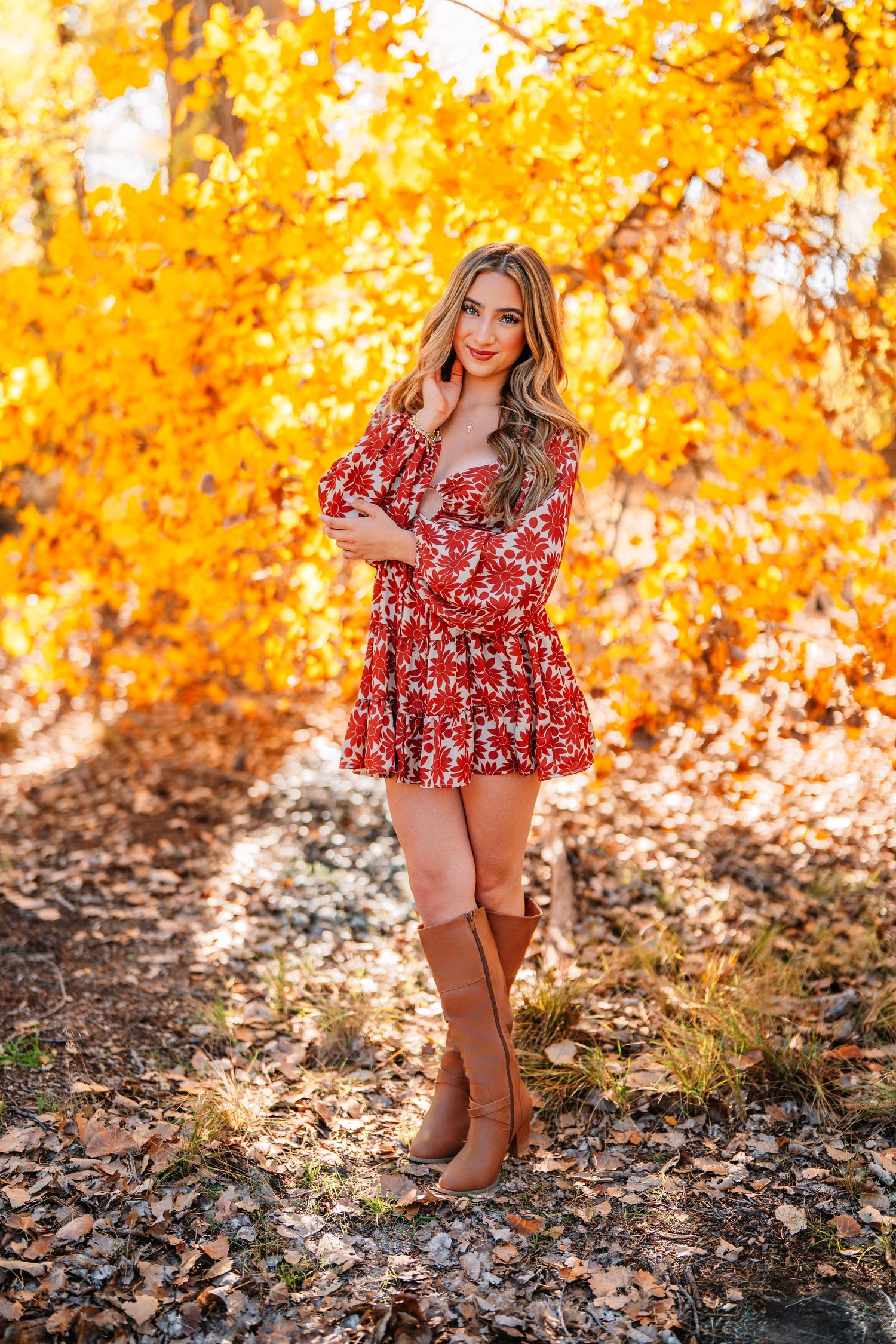 A fall fashion portrait featuring a red floral dress and brown boots against golden autumn foliage.