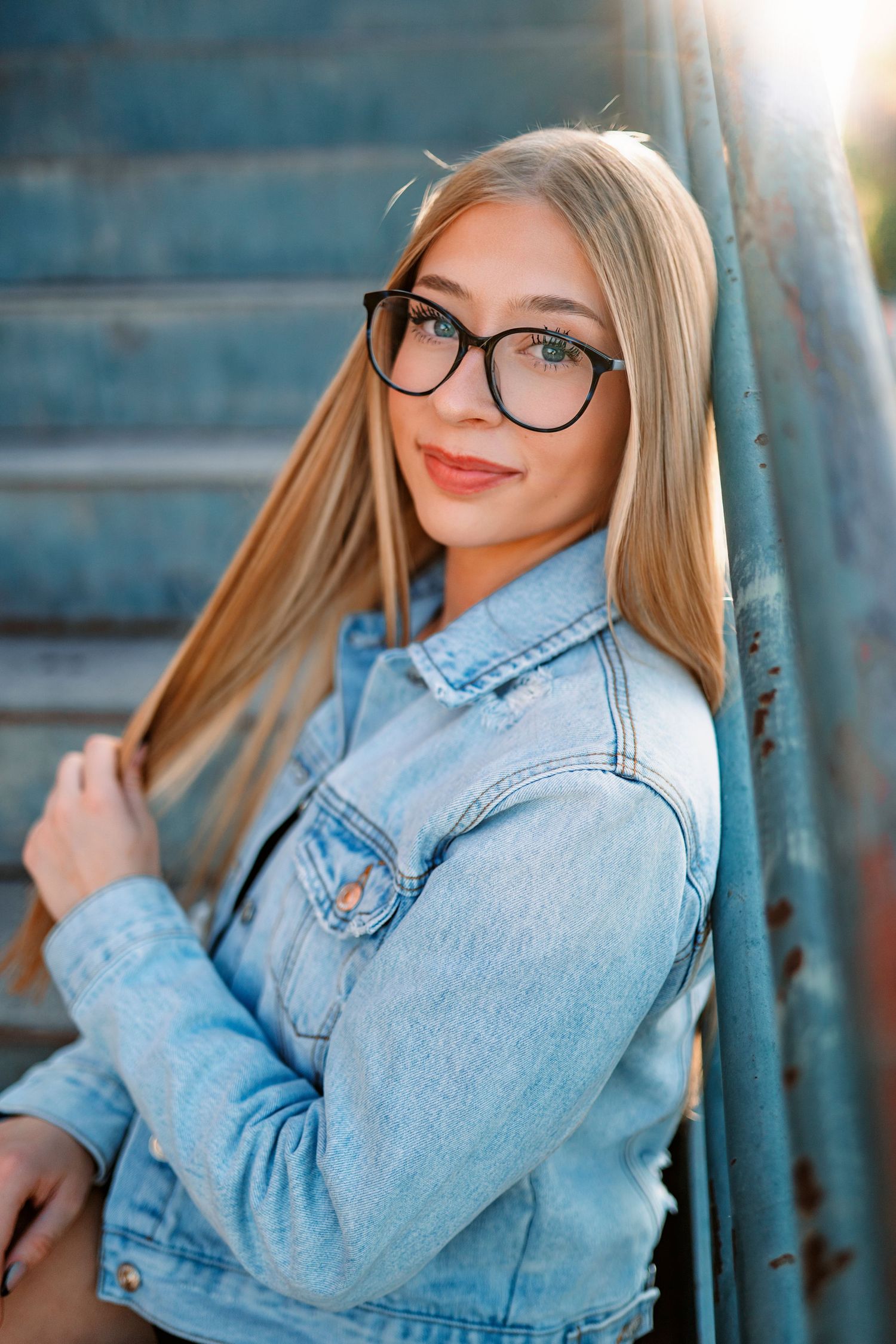 Portrait in denim jacket and glasses against blue background with soft natural lighting.