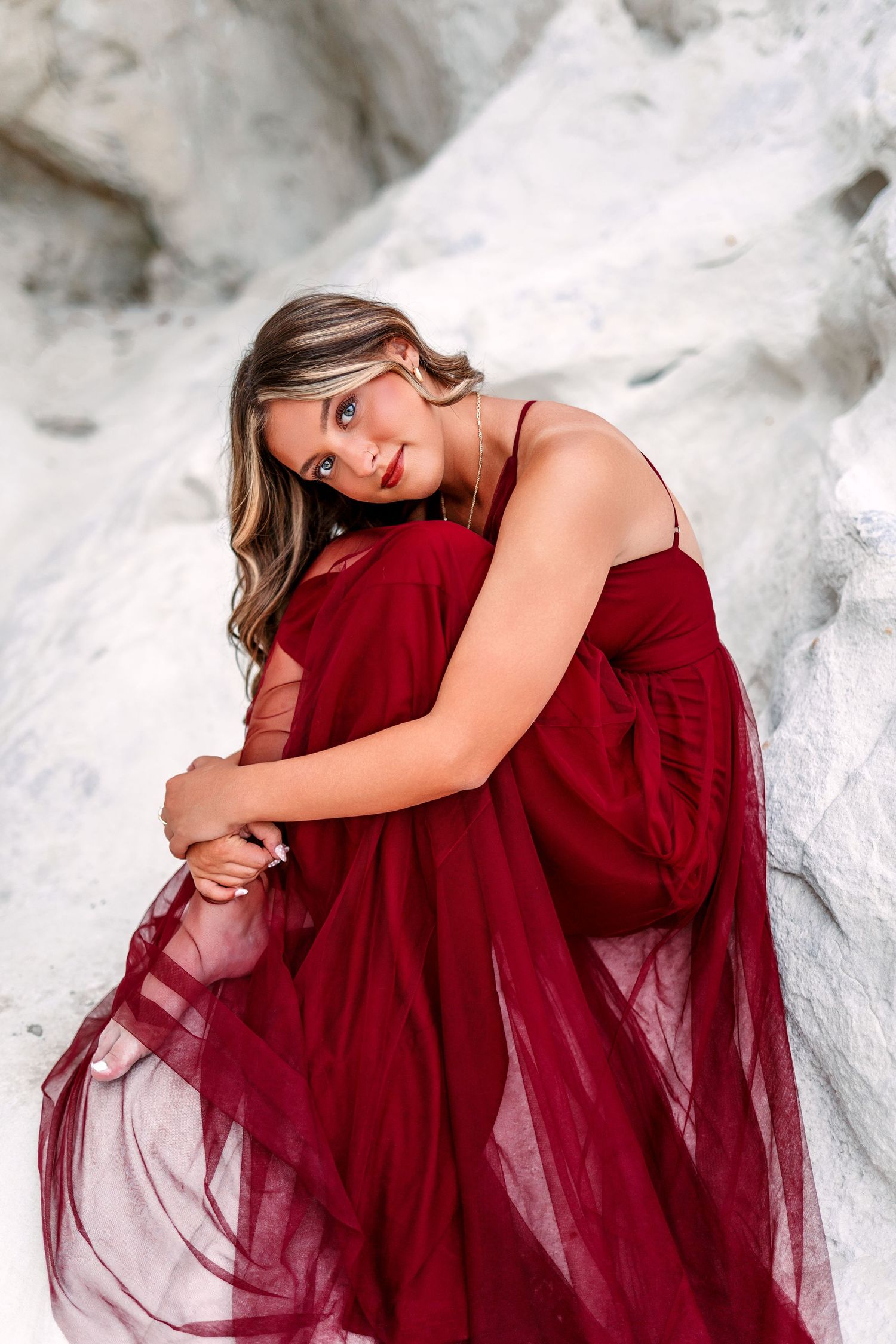 Woman in burgundy tulle dress poses against white rock formation.