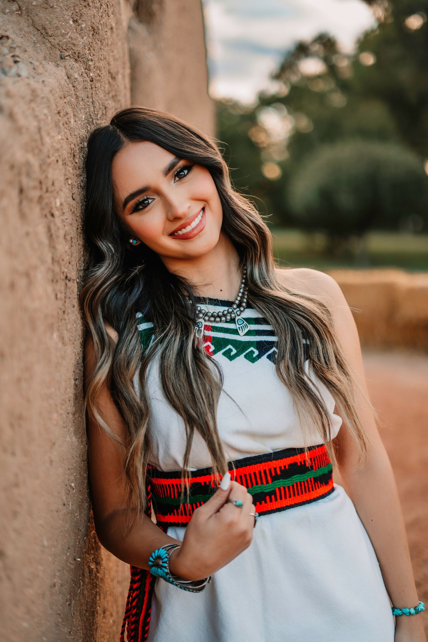 Southwestern style portrait series against adobe wall with traditional accessories.