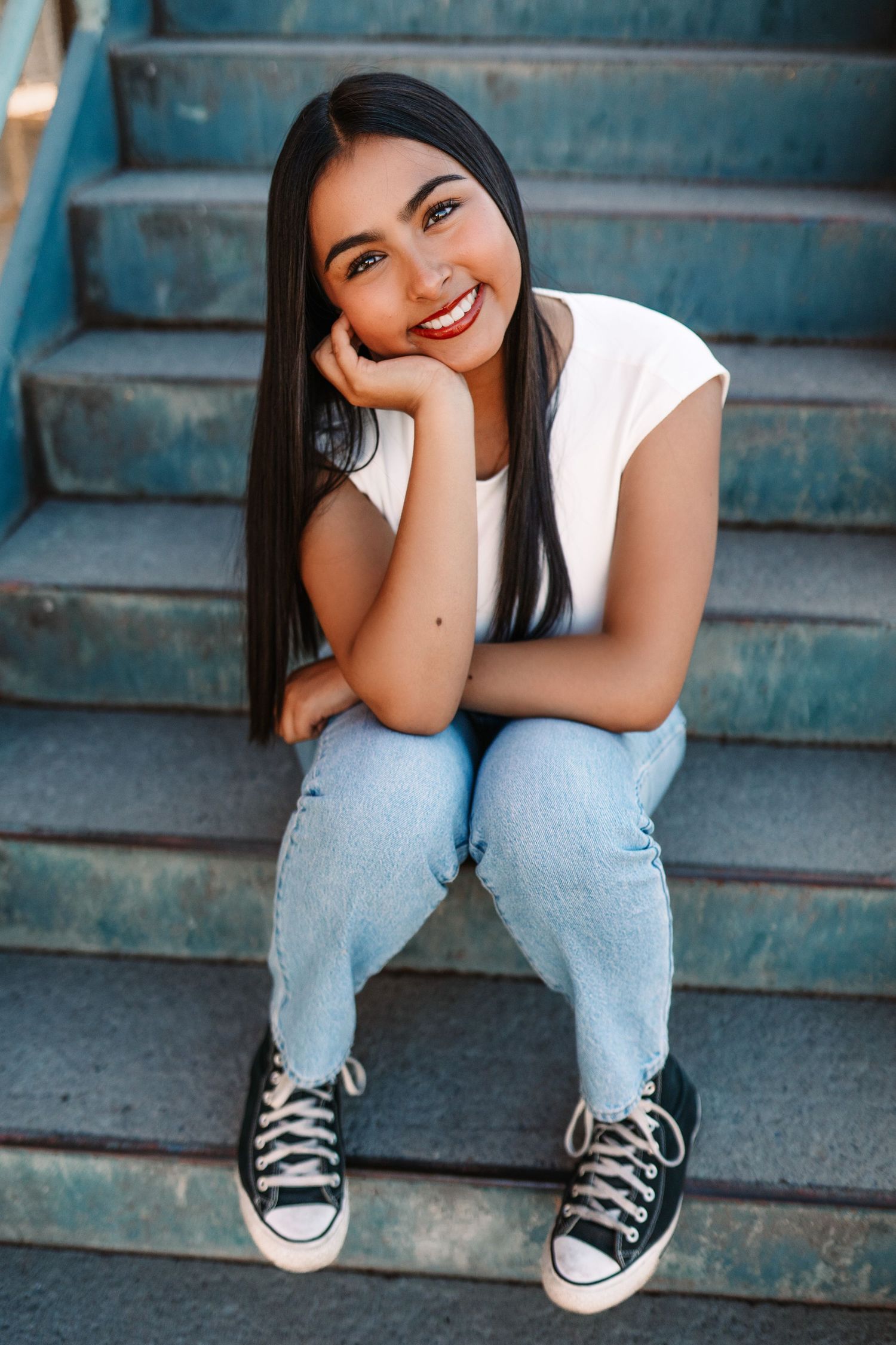 Casual portraits on blue steps wearing white top, jeans and classic black sneakers.