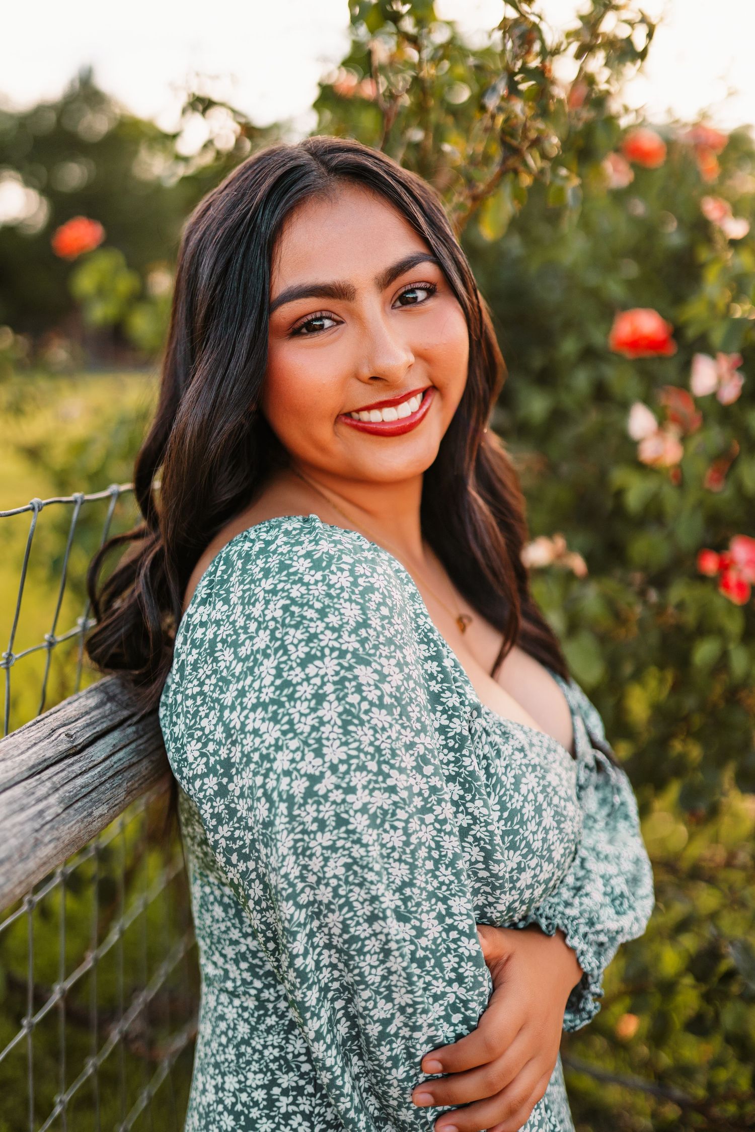 Portrait in floral green dress against garden background with roses.
