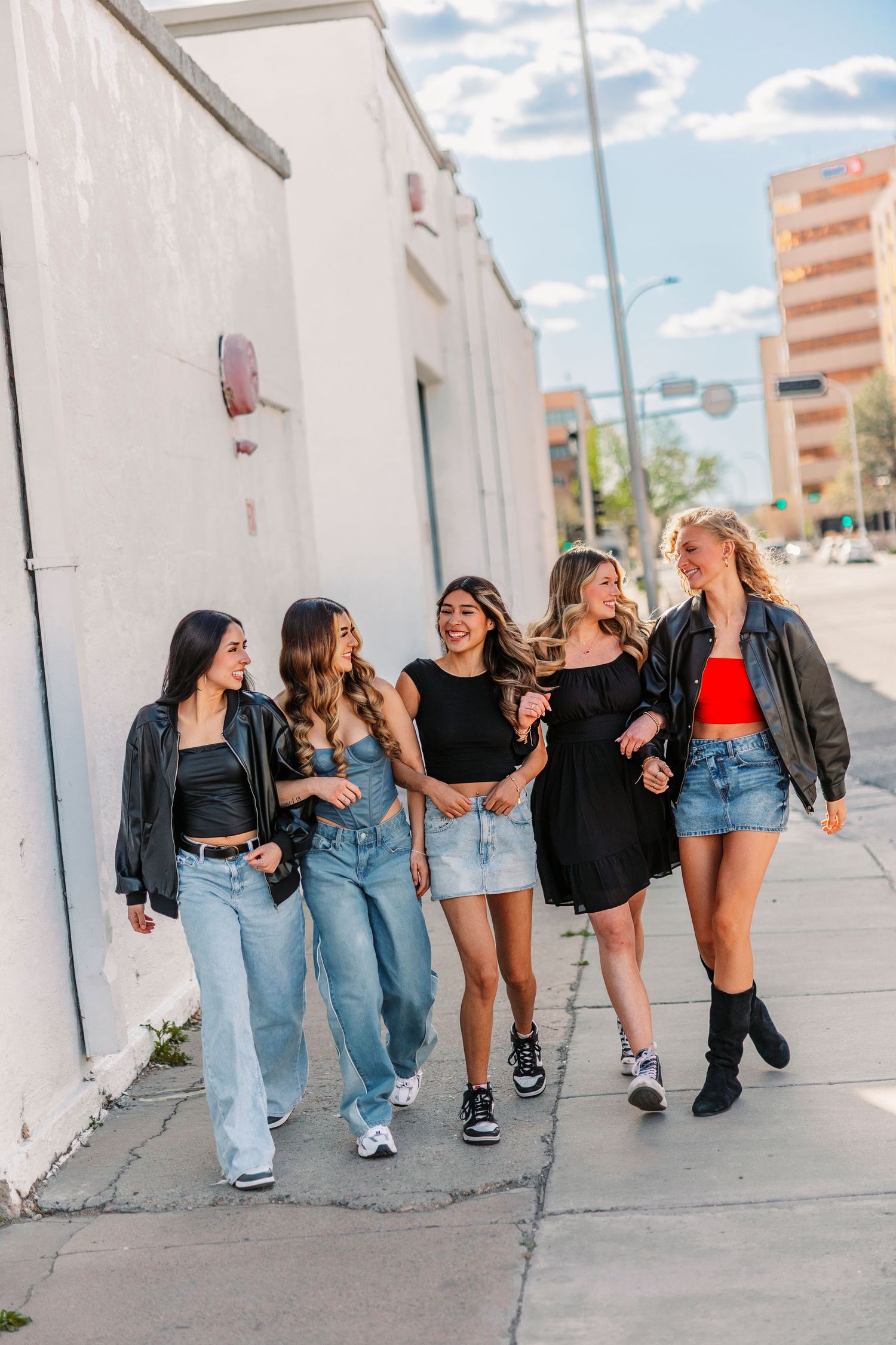 Friends in coordinated outfits lean against white wall during urban photoshoot.