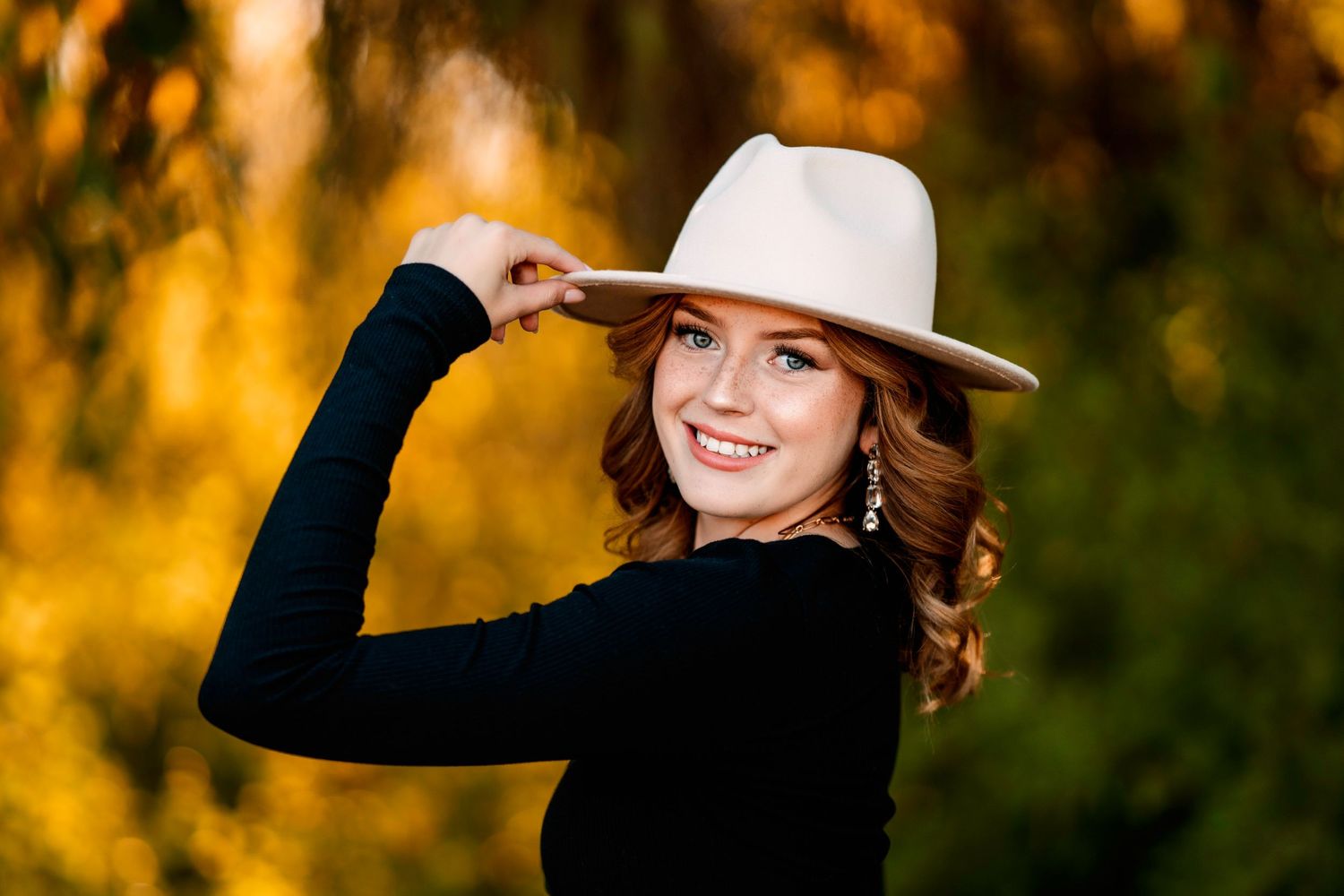 Autumn portrait session in a golden sunlit field with a wide-brimmed hat creating a warm, natural aesthetic.