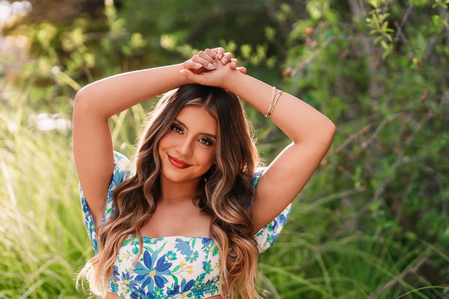Woman in blue floral summer outfit poses with hands above head.