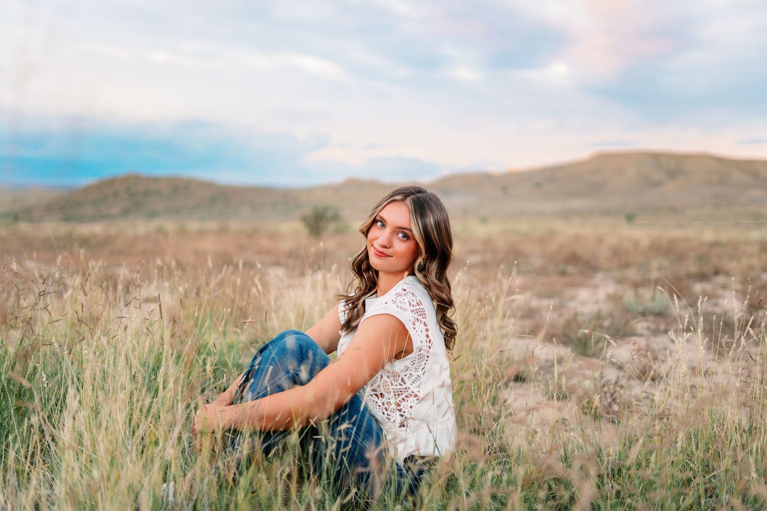 Woman in lace top sits thoughtfully in golden mountain field.