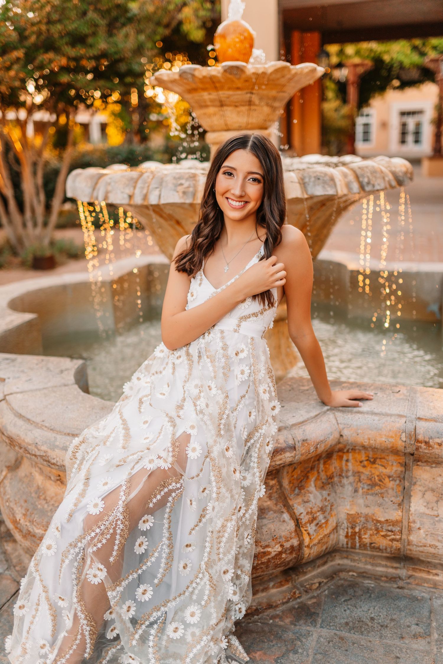 Elegant portraits by fountain wearing white lace dress at golden hour.