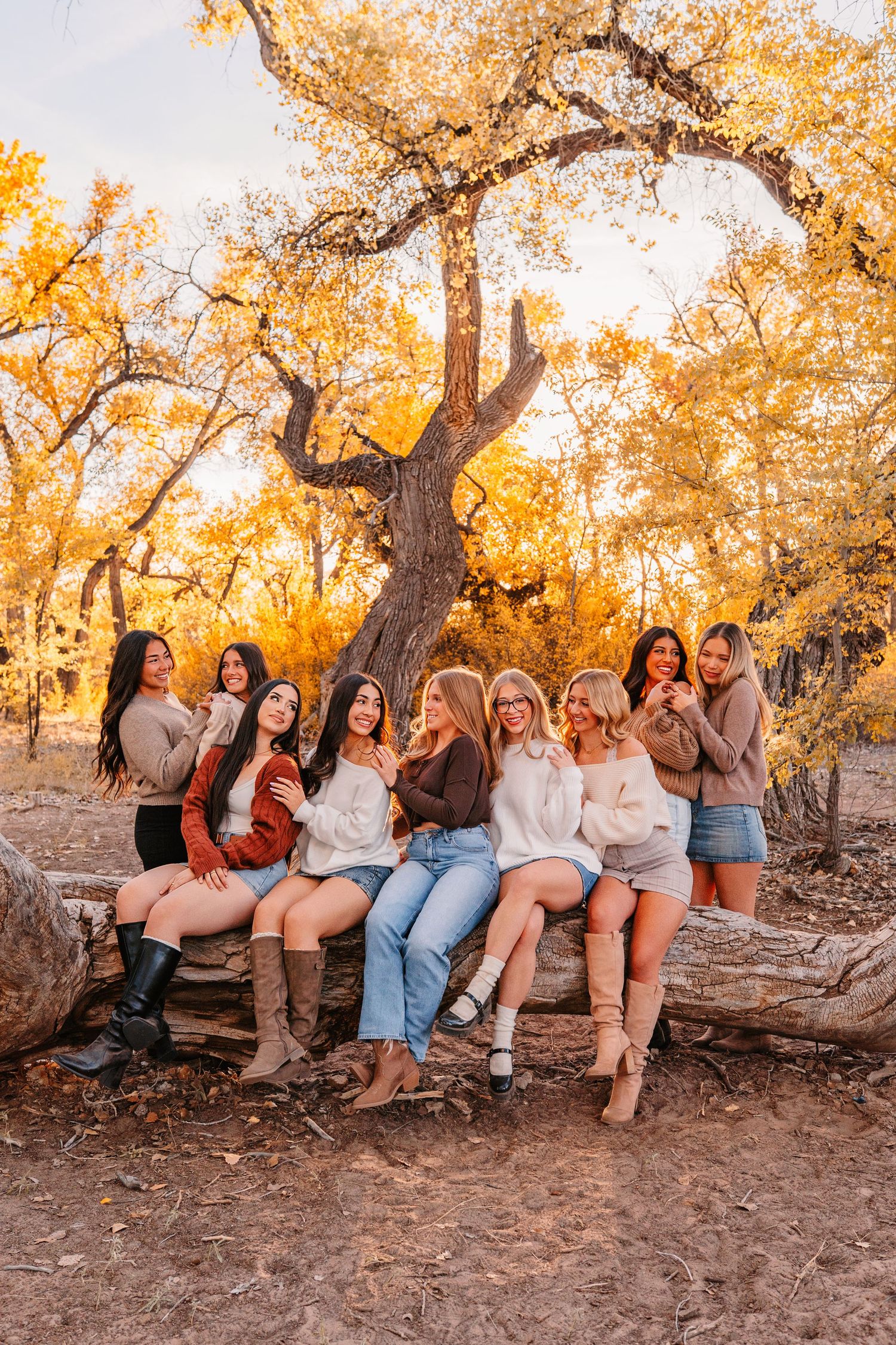 Friends relaxing on fallen tree trunk surrounded by golden autumn leaves.