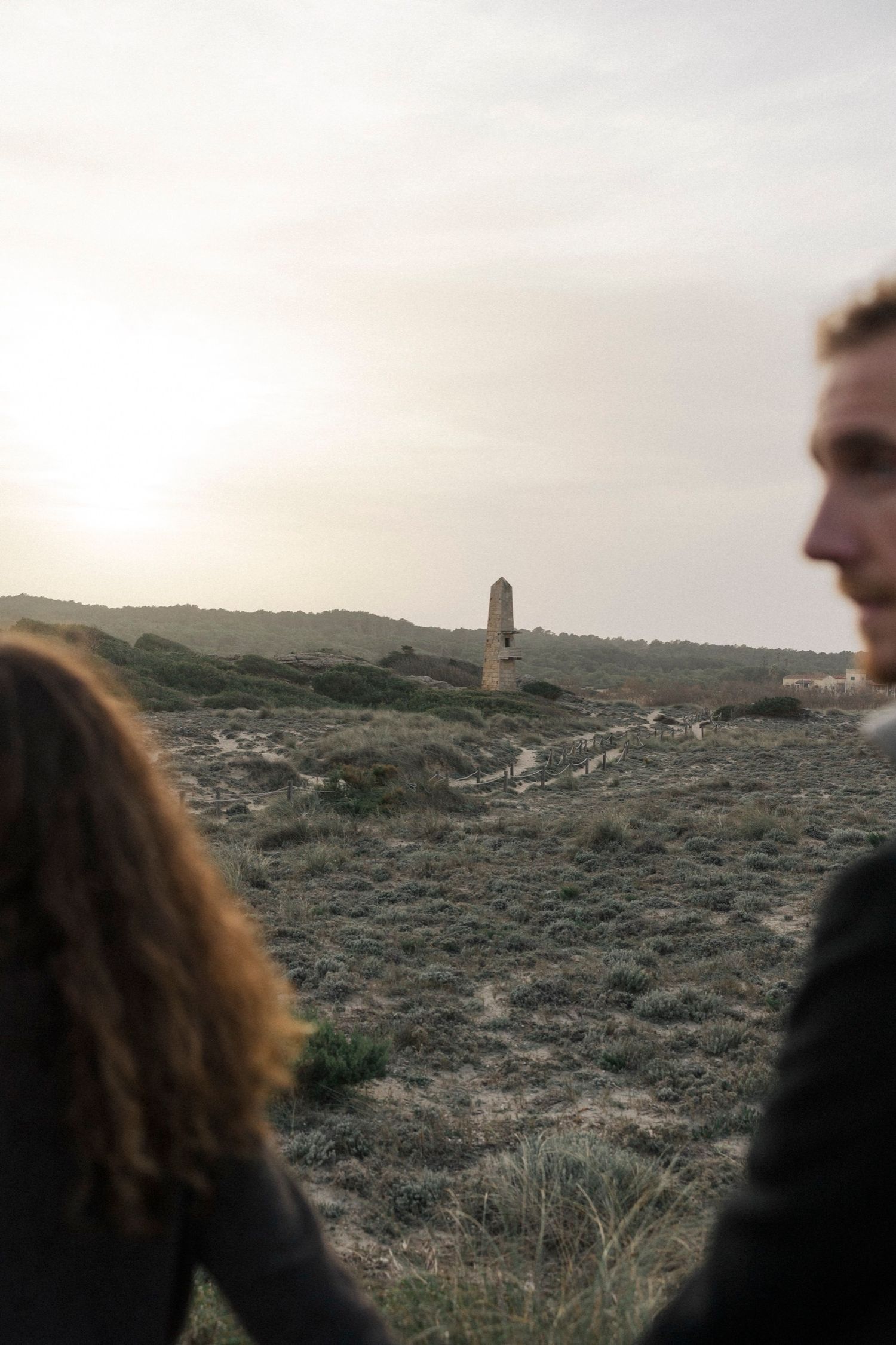 People look out over a rugged hillside landscape with a distant tower or structure visible on the horizon.