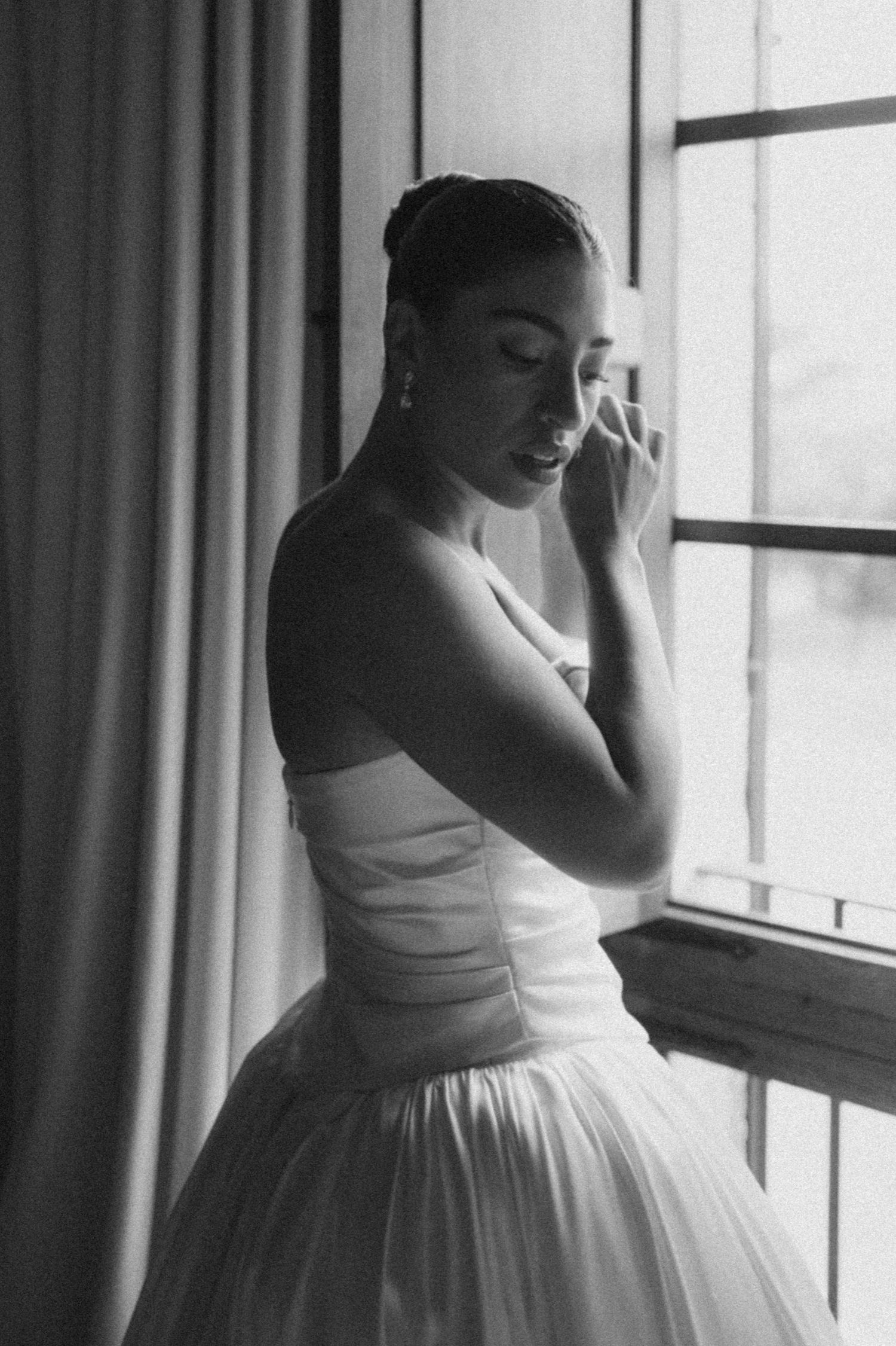 Black and white photos showing the elegant details of a wedding dress near a bright window.
