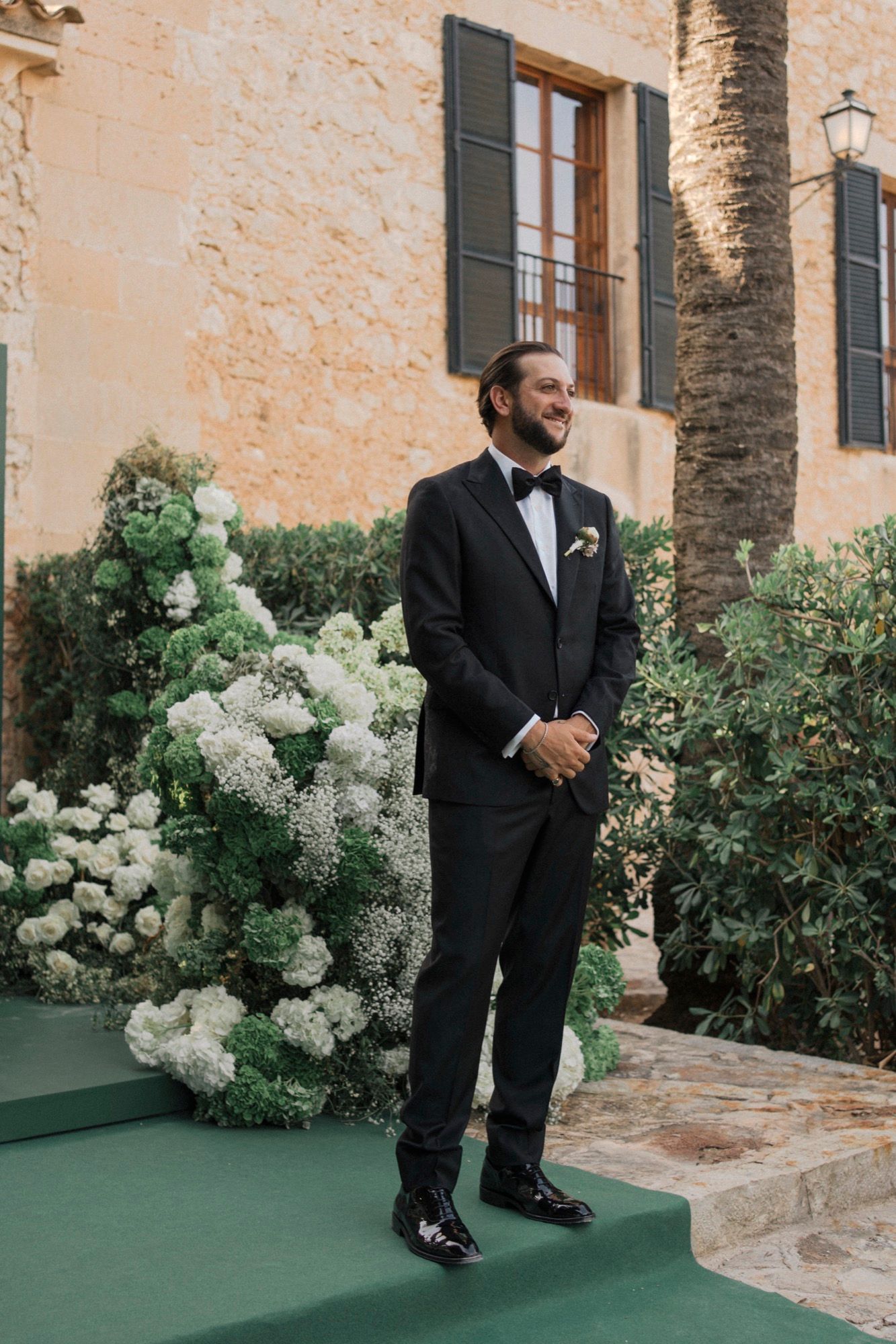 Wedding ceremony setting with white floral arrangements against a stone building facade.