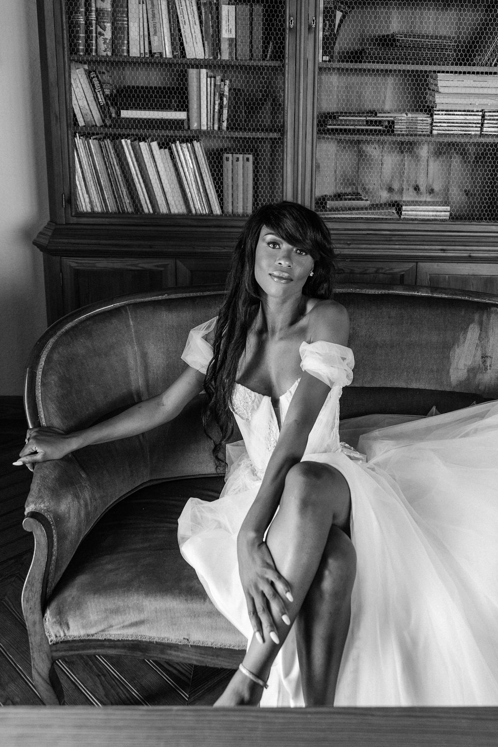 Artistic black and white bridal portrait on vintage leather couch with bookshelves.