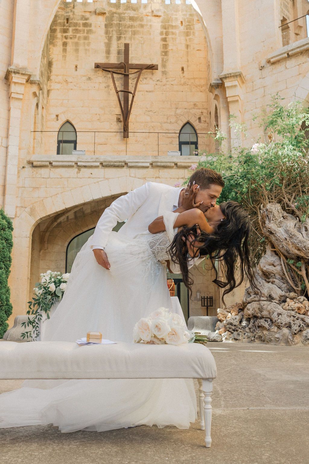 Playful wedding photo session on bench in historic stone church courtyard.