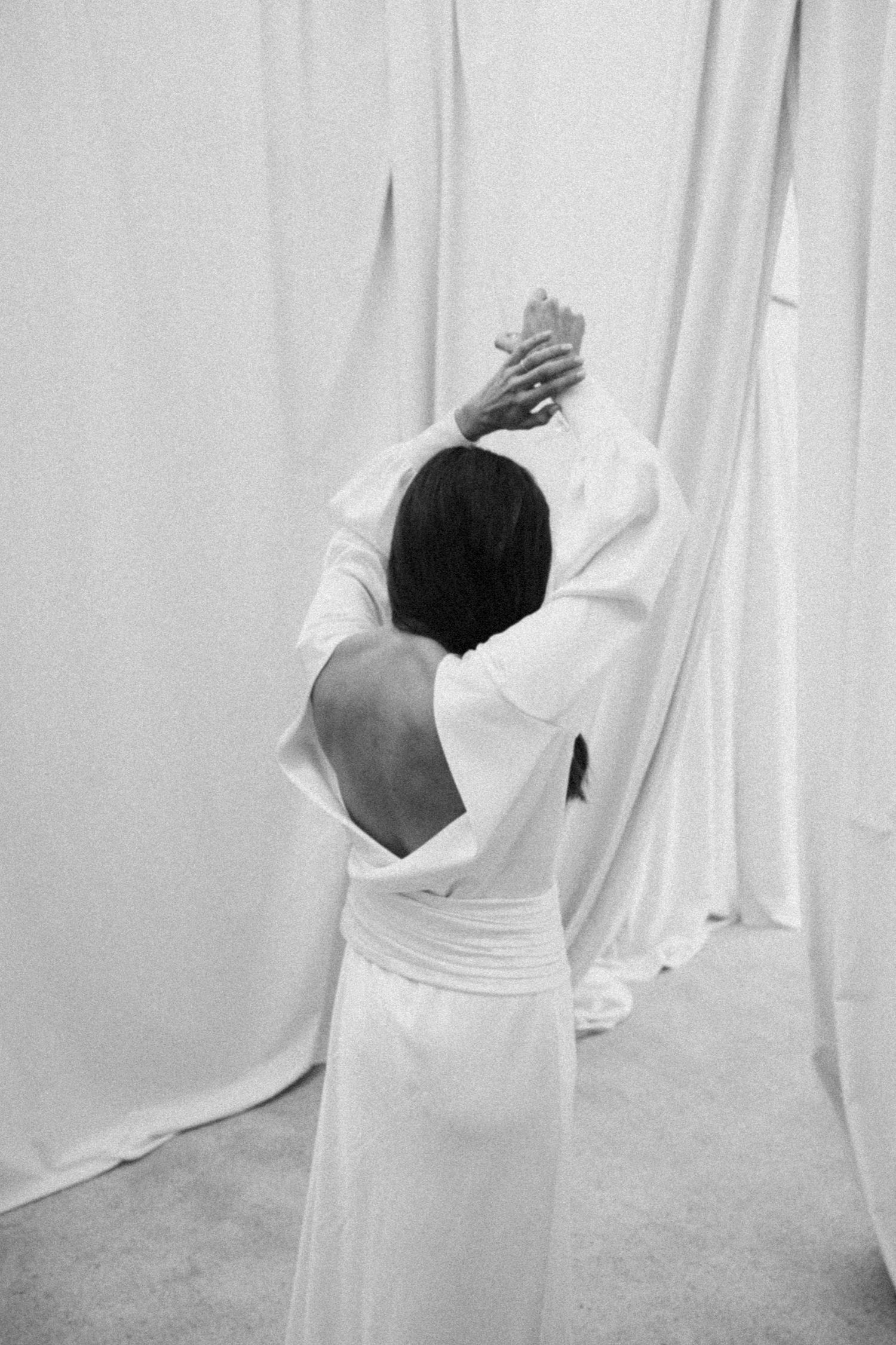 Abstract dance-like movements captured in black and white against white curtain backdrop.