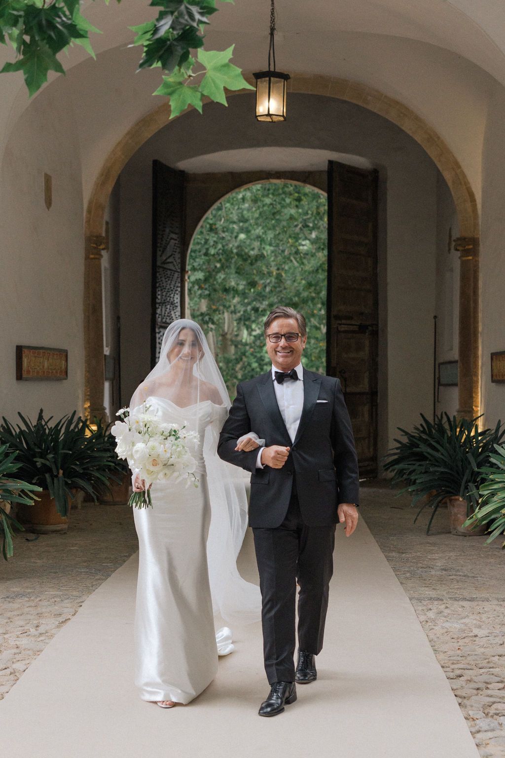 A wedding couple walks down an elegant hallway with arched ceilings and hanging lanterns.