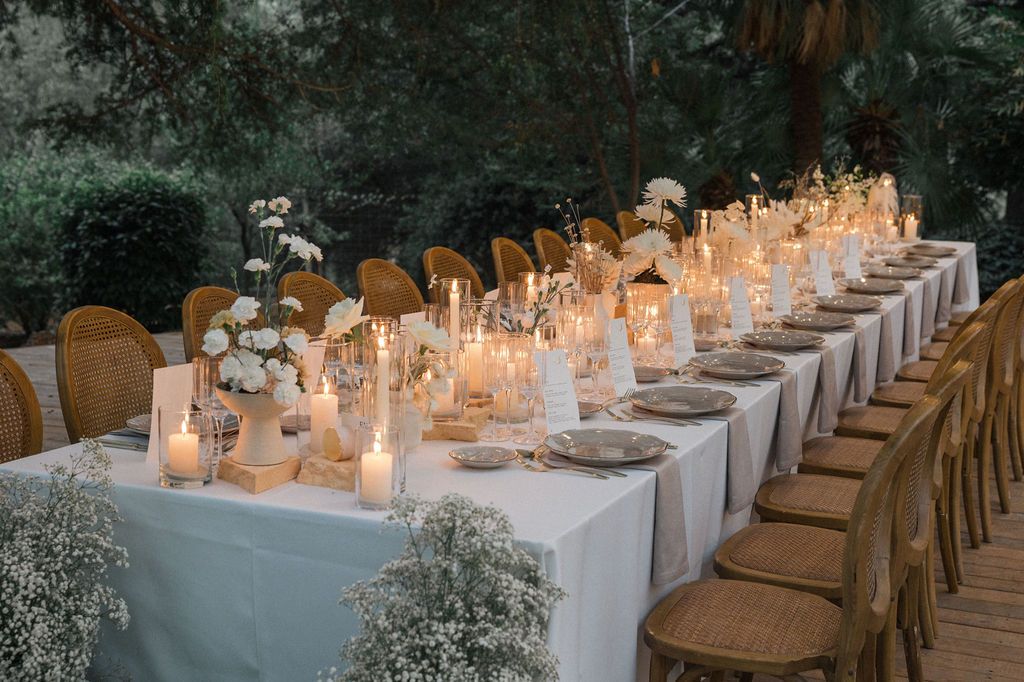 Long banquet tables with white linens and wooden chairs set for outdoor wedding reception.
