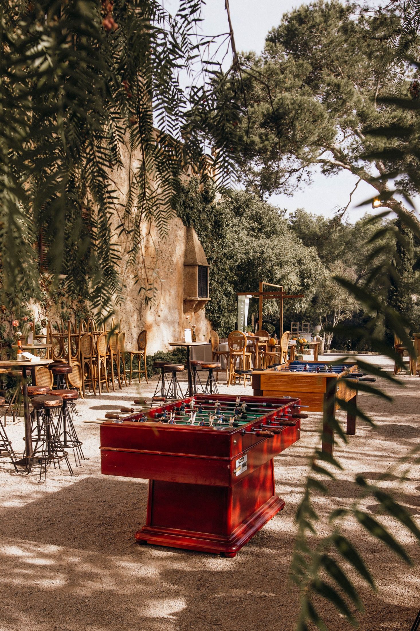Red wooden benches arranged in rows under shady trees at an outdoor wedding venue with rustic decor.
