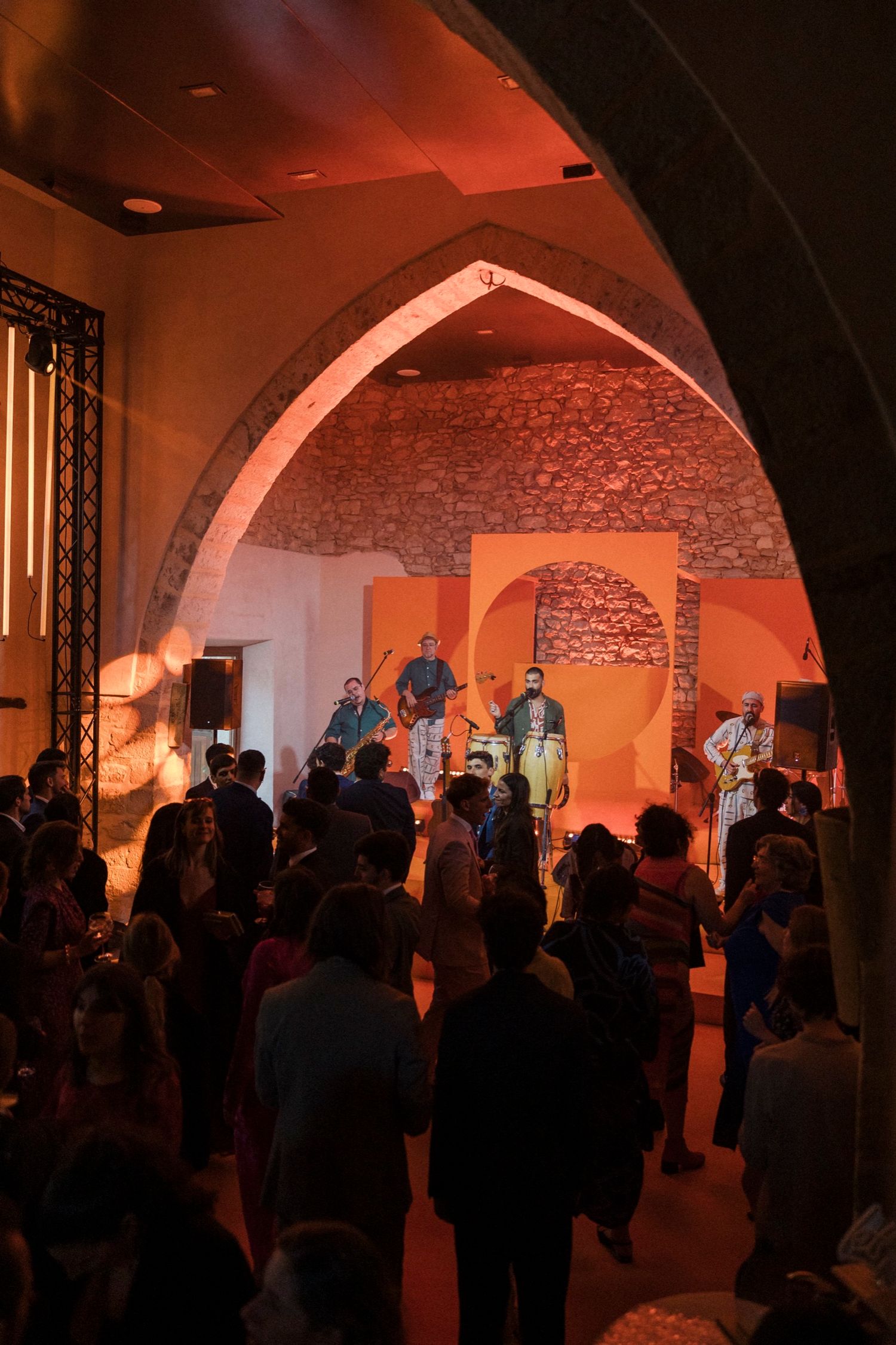 Crowded underground venue with brick arches and orange ambient lighting showing silhouettes of people gathered.